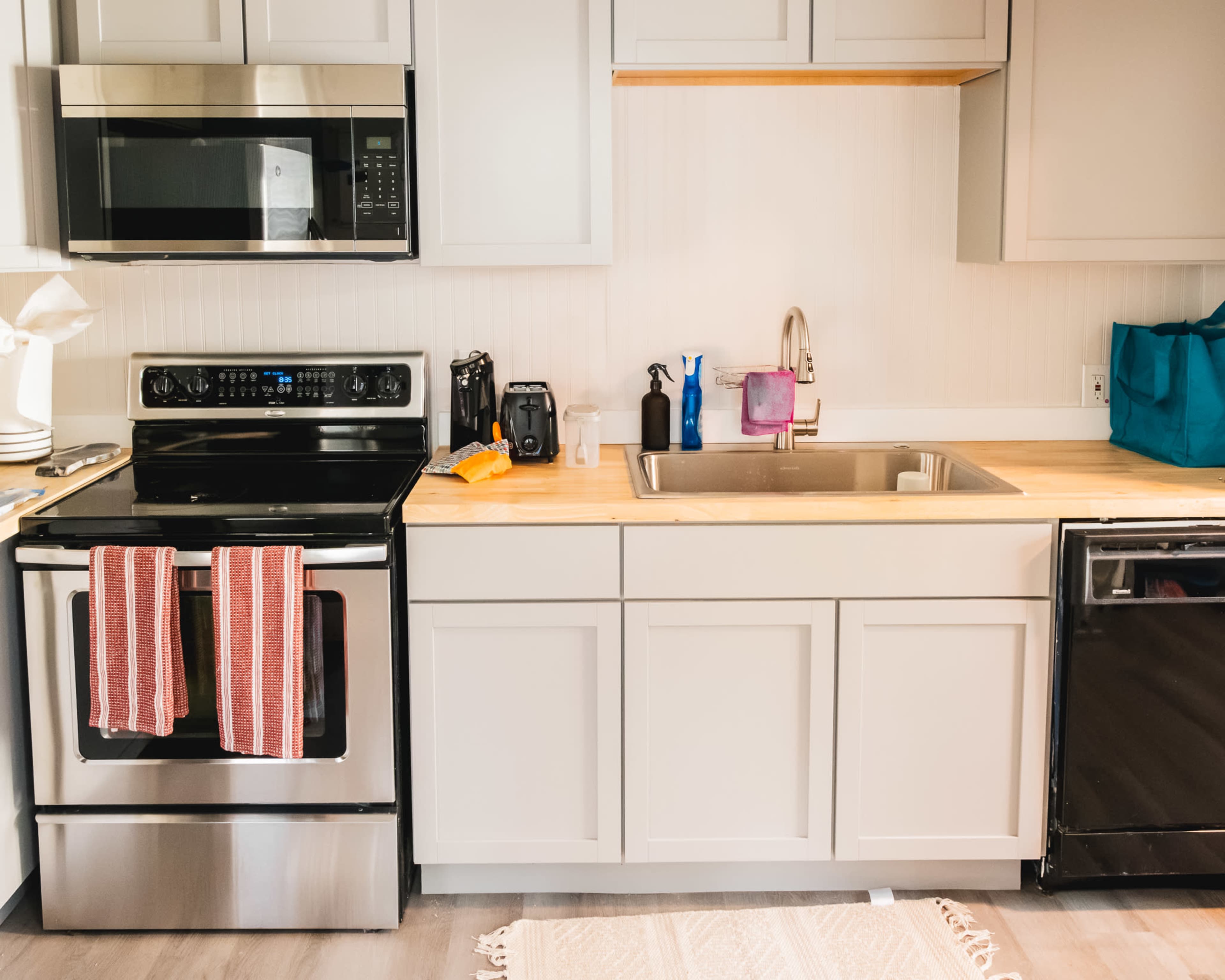 A modern kitchen features stainless steel appliances, a wooden countertop, and a sink, with red-striped towels hanging from the stove.