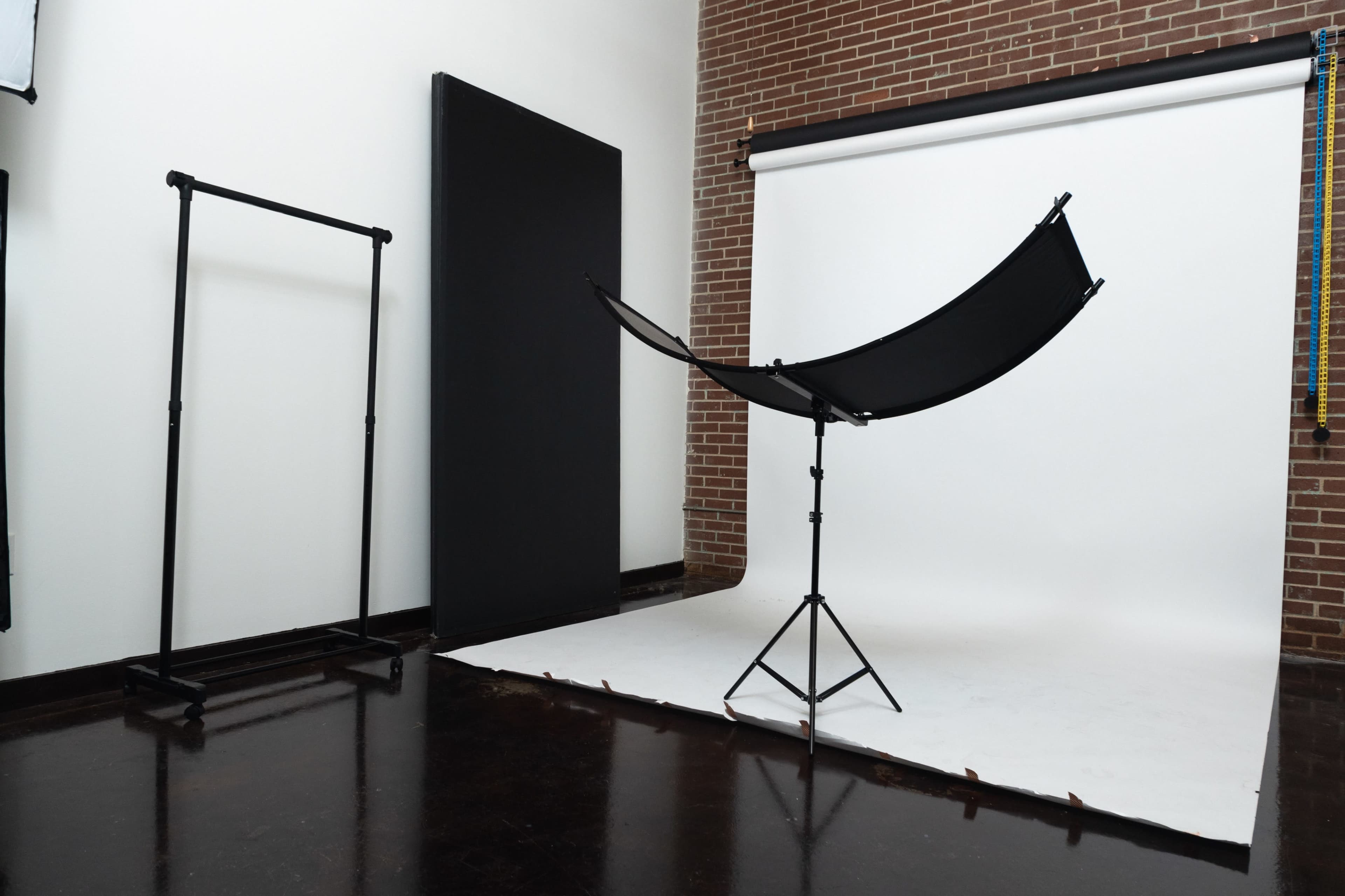 A photography studio with a backdrop, a large black reflector on a stand, and an equipment rack.