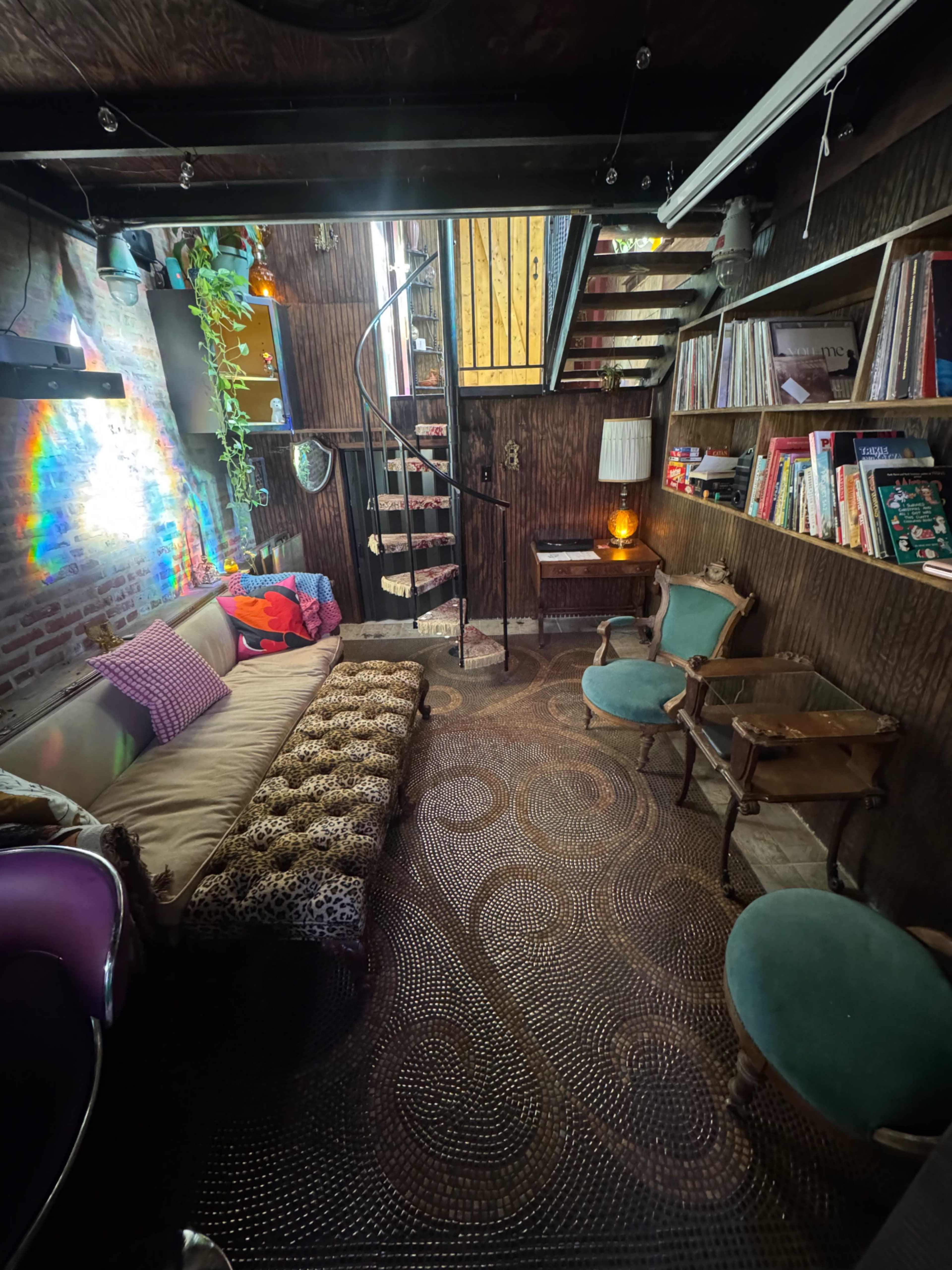 The room features a spiral staircase leading up, surrounded by bookshelves, seating areas, and decorative plants.