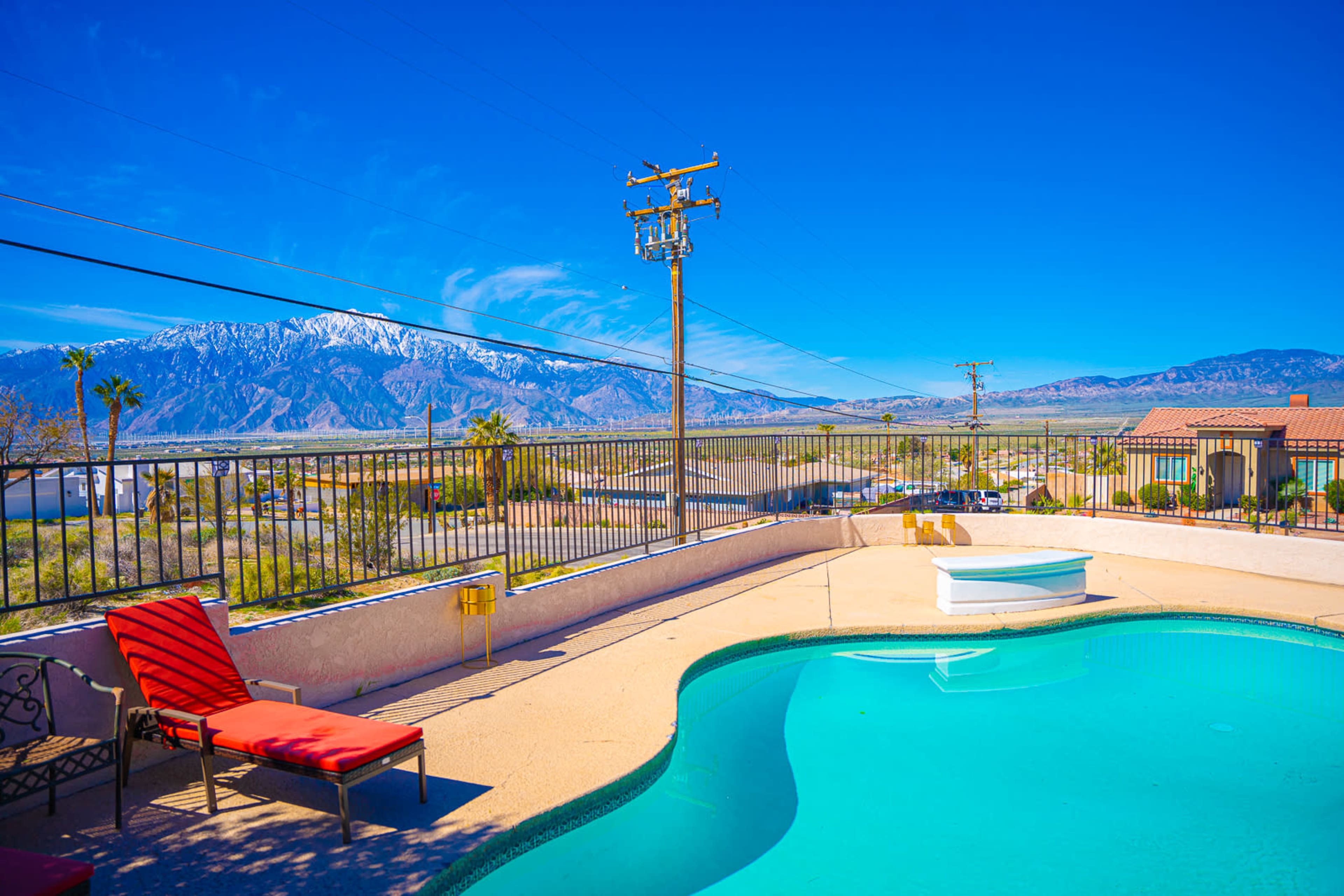 A swimming pool with red loungers overlooking a mountainous landscape under a clear blue sky.