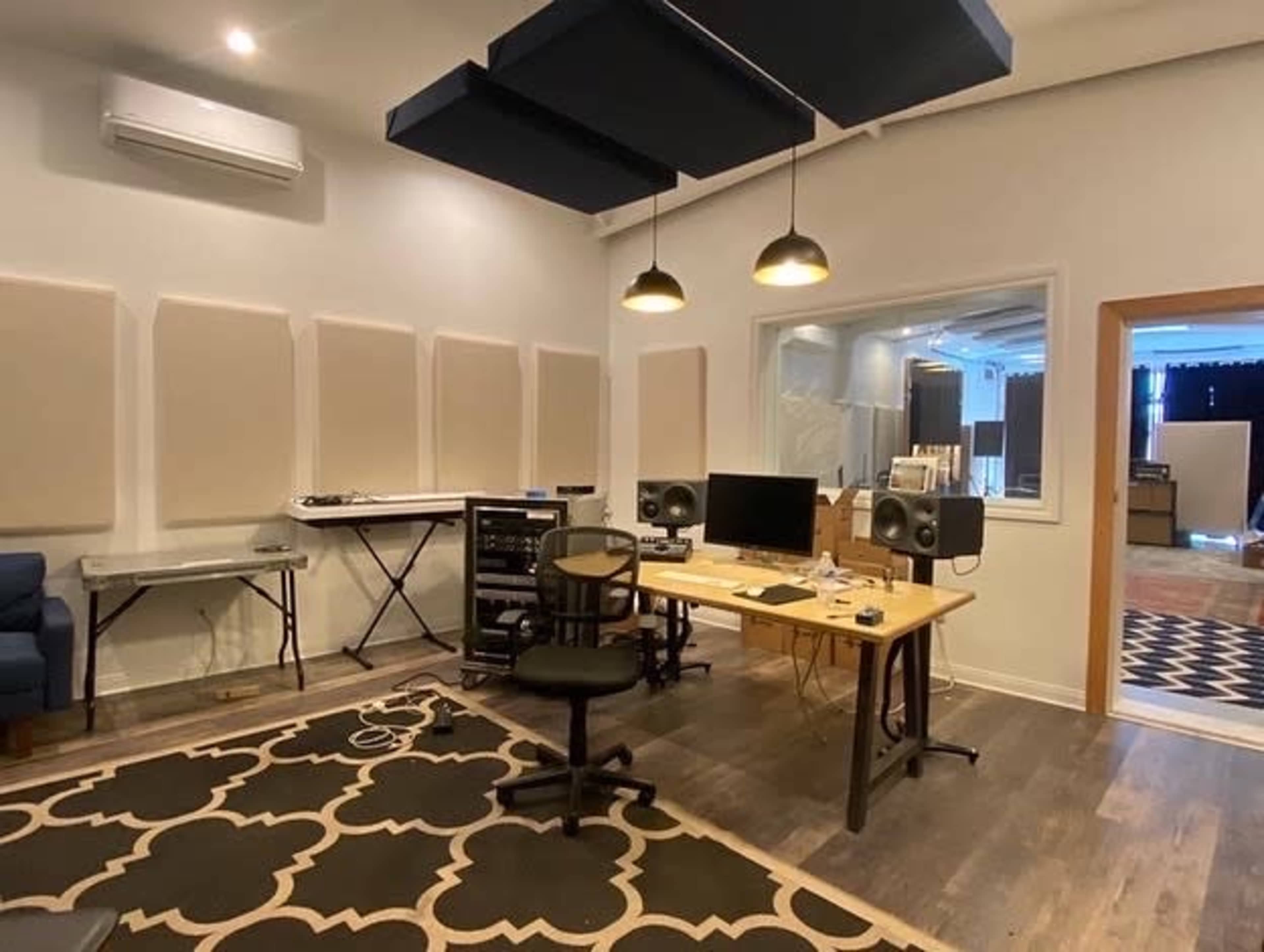 A music studio with soundproof panels on the walls, a wooden desk with a computer and speakers, and a chair in front of the desk.