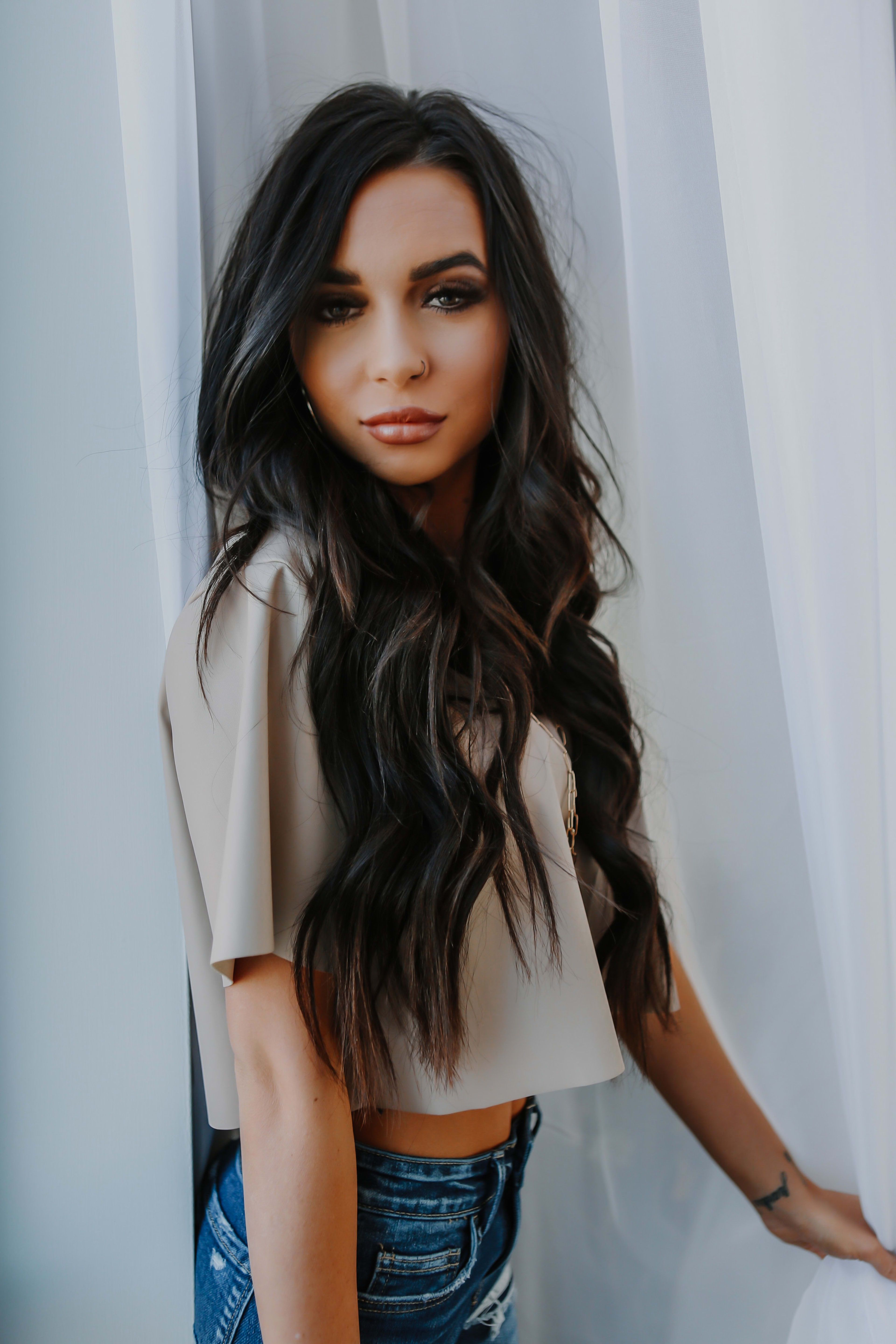 A woman with long dark hair standing in front of a white curtain for a head shot portrait.