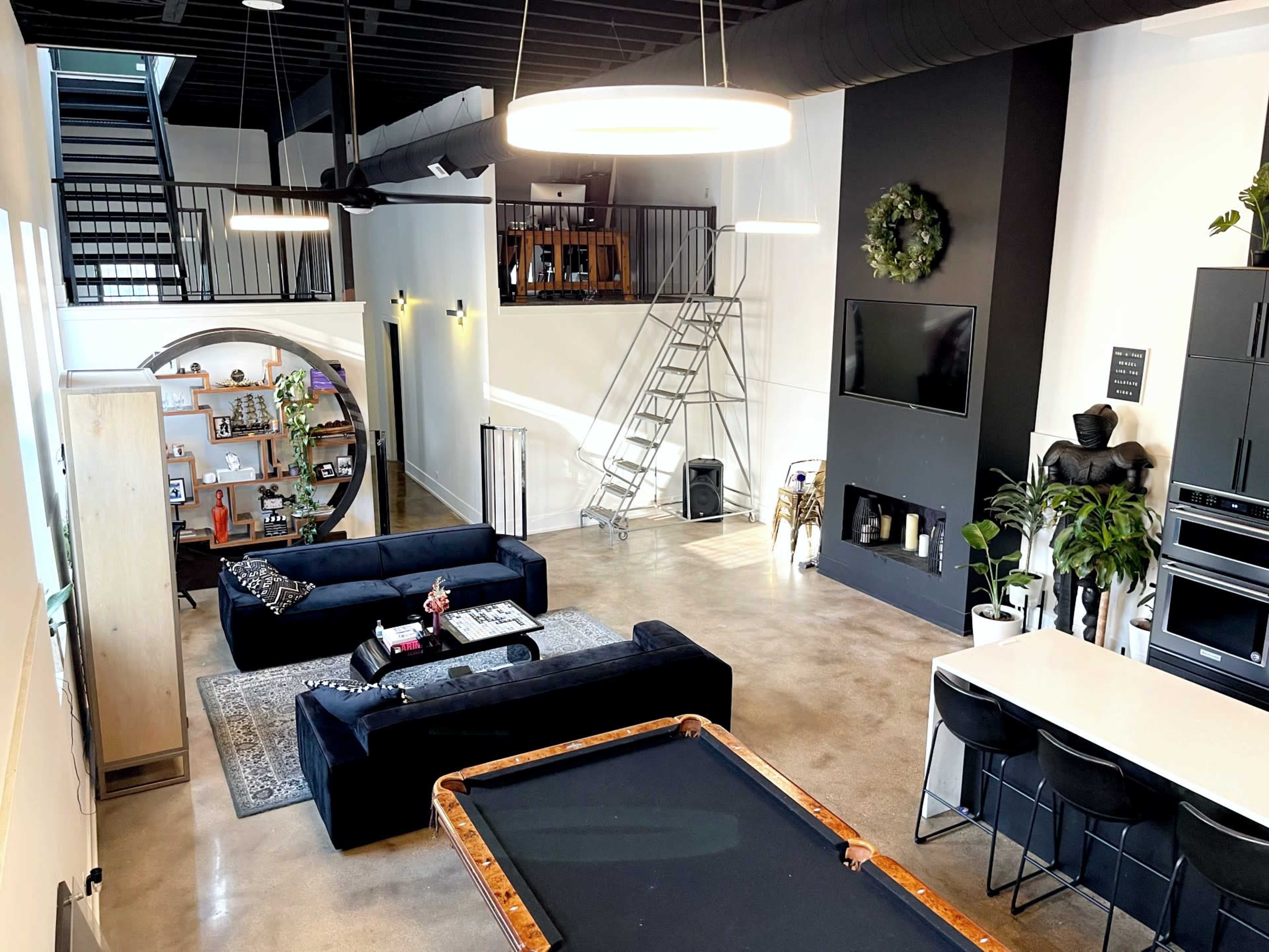 A spacious loft-style living area featuring a modern kitchen, a pool table, and large windows that illuminate the space.