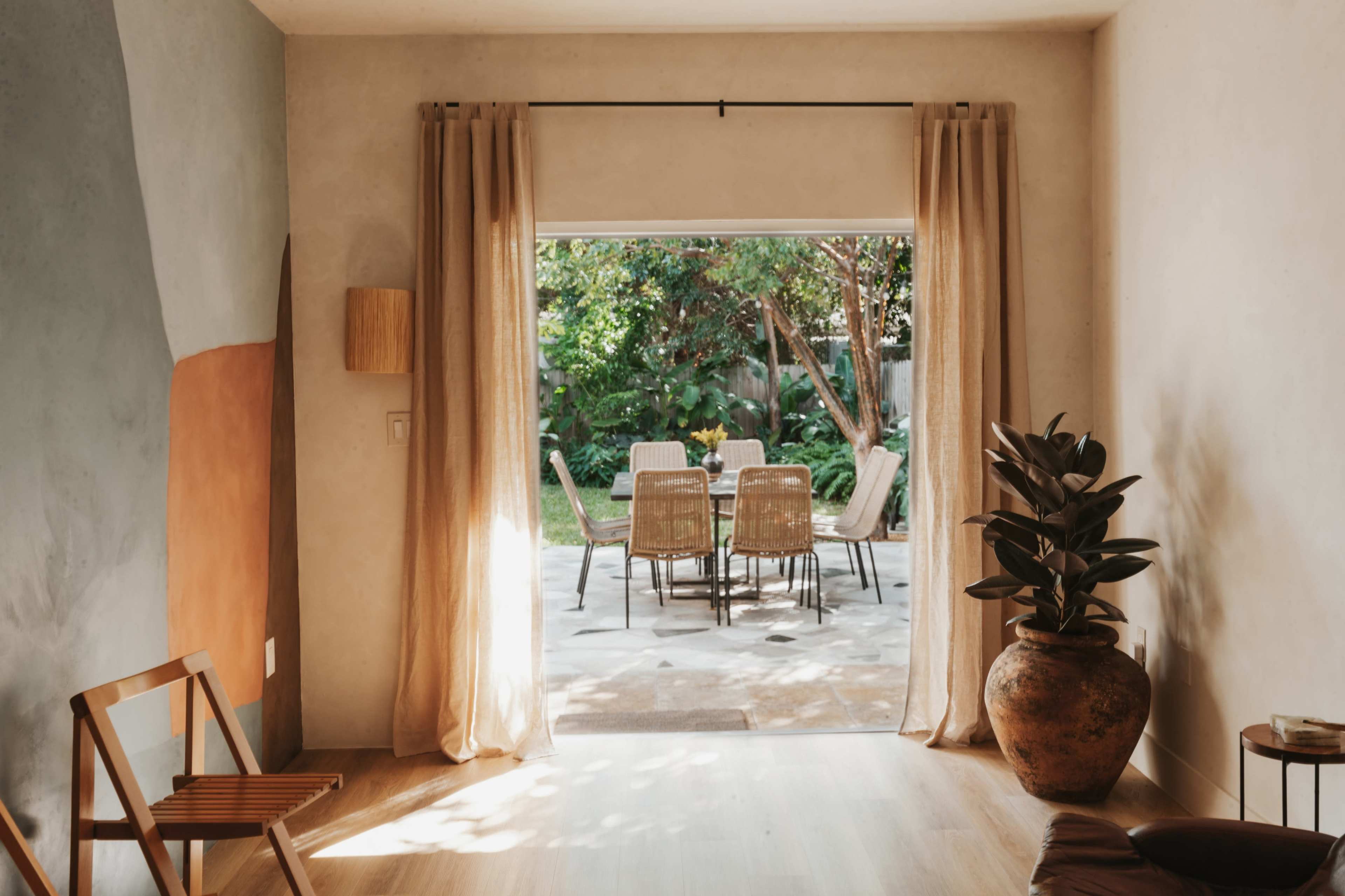 A spacious living area opens to a patio with a dining set surrounded by greenery.