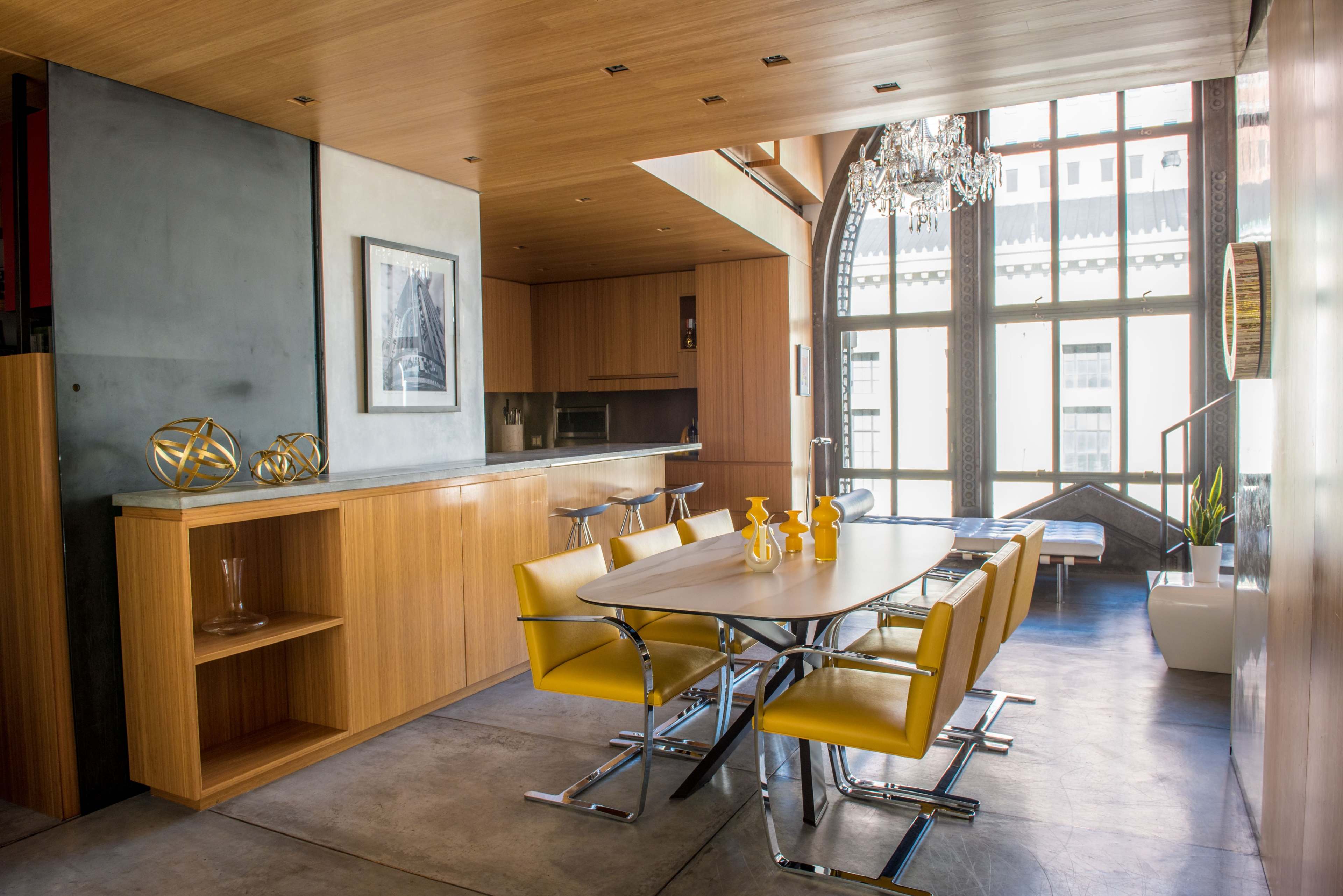 A modern dining area featuring a sleek table with yellow chairs, surrounded by large windows that allow natural light to fill the space.
