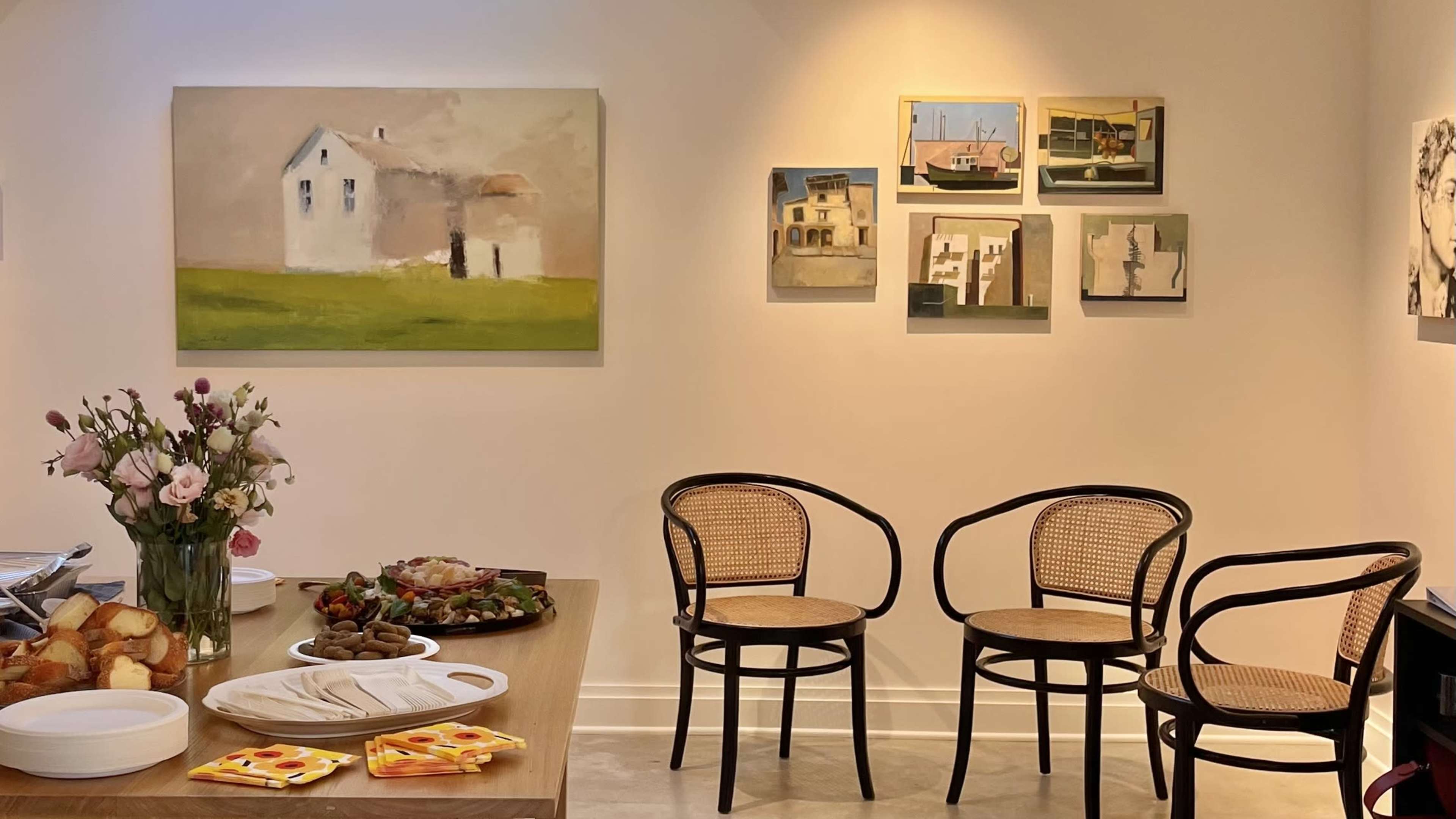 The scene features a dining table with food, a vase of flowers, and several framed artworks on the wall opposite a set of two empty chairs.