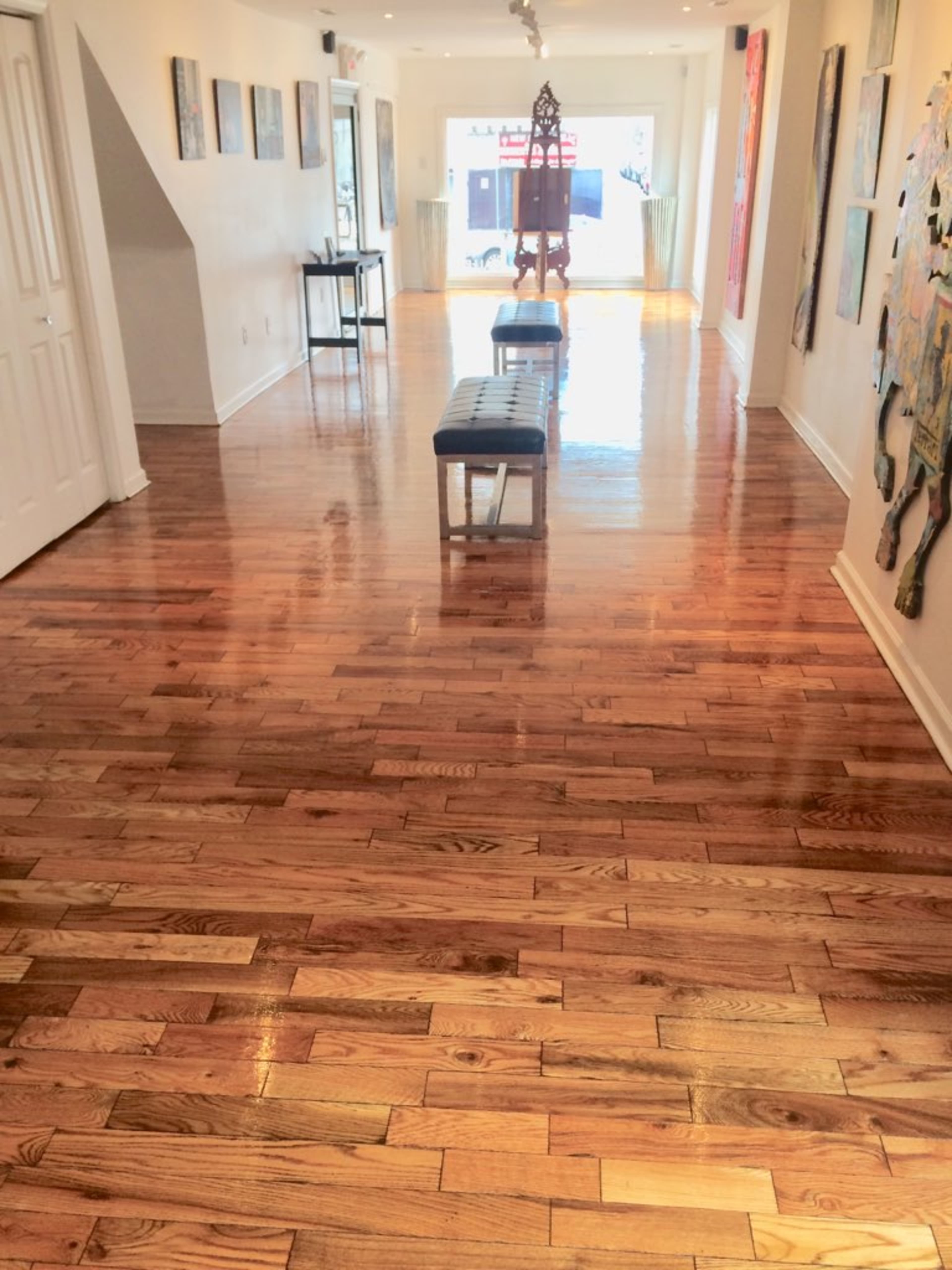 The hallway features polished wooden floors, with artwork displayed on the walls and a bench seating area in the center.