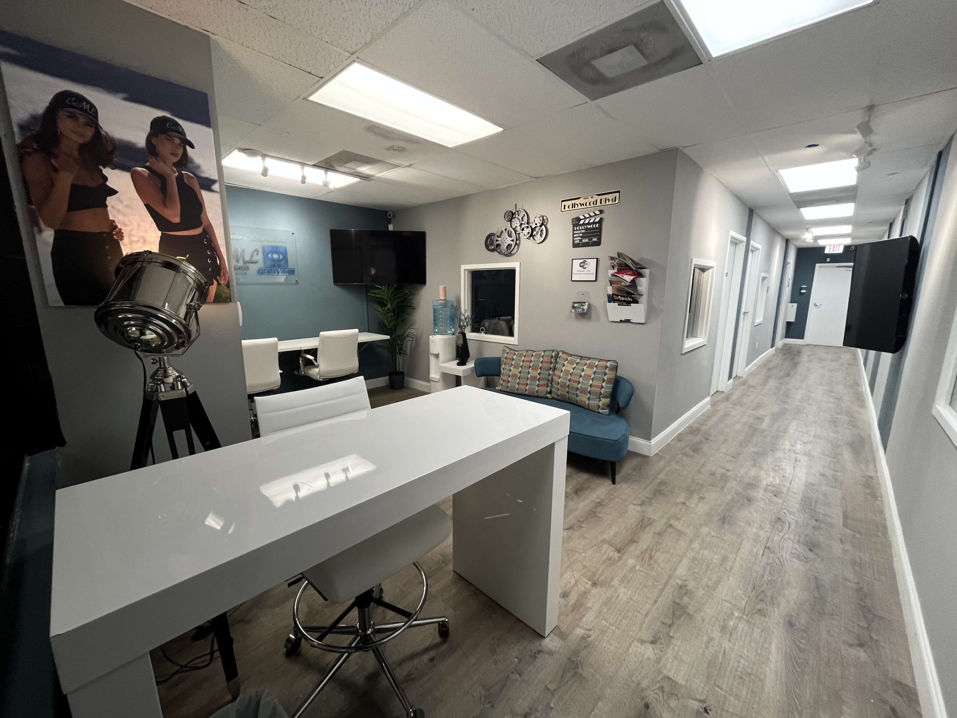 A modern office hallway featuring a white desk, seating area with a couch, and framed artwork on the walls.