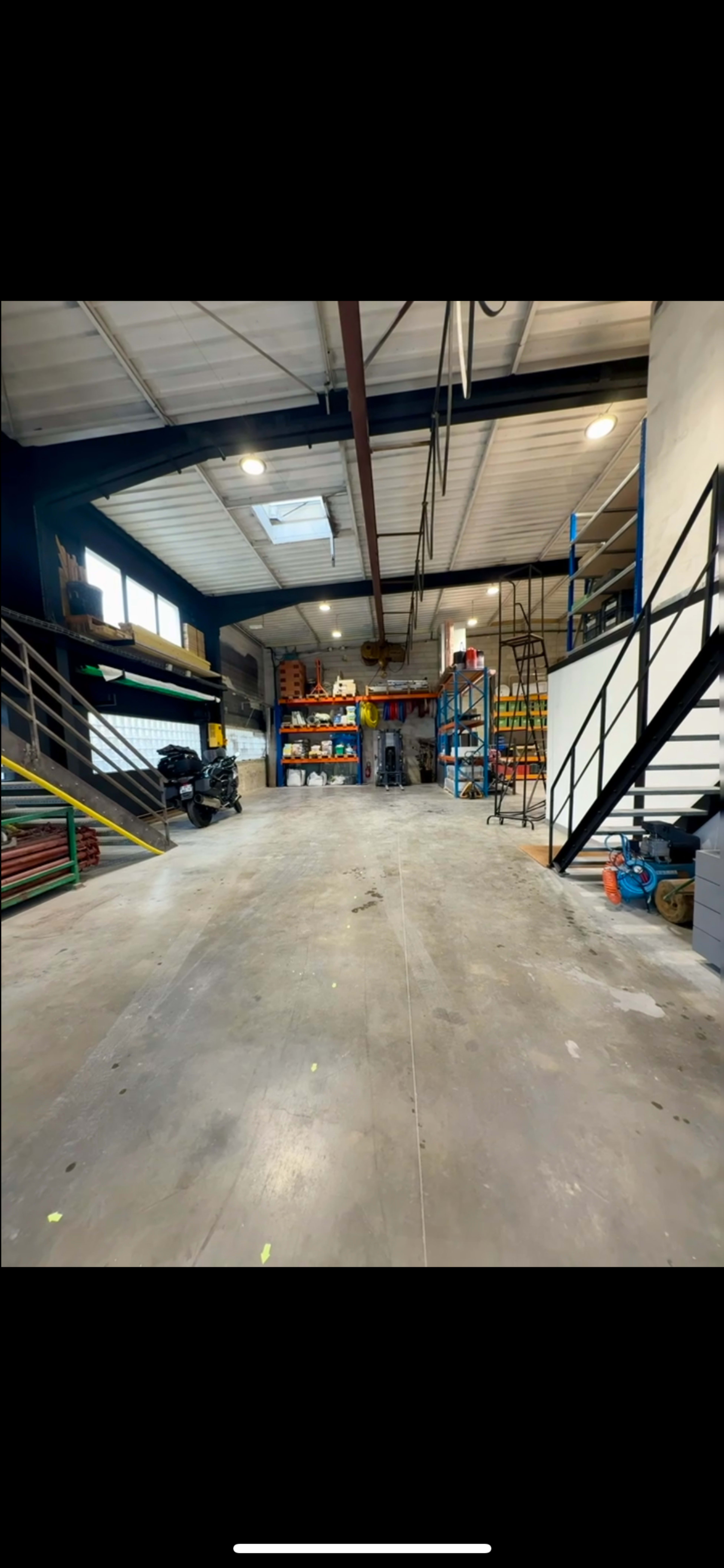 The image shows an industrial warehouse interior with shelving units, a staircase, and various tools and equipment arranged neatly along the sides.