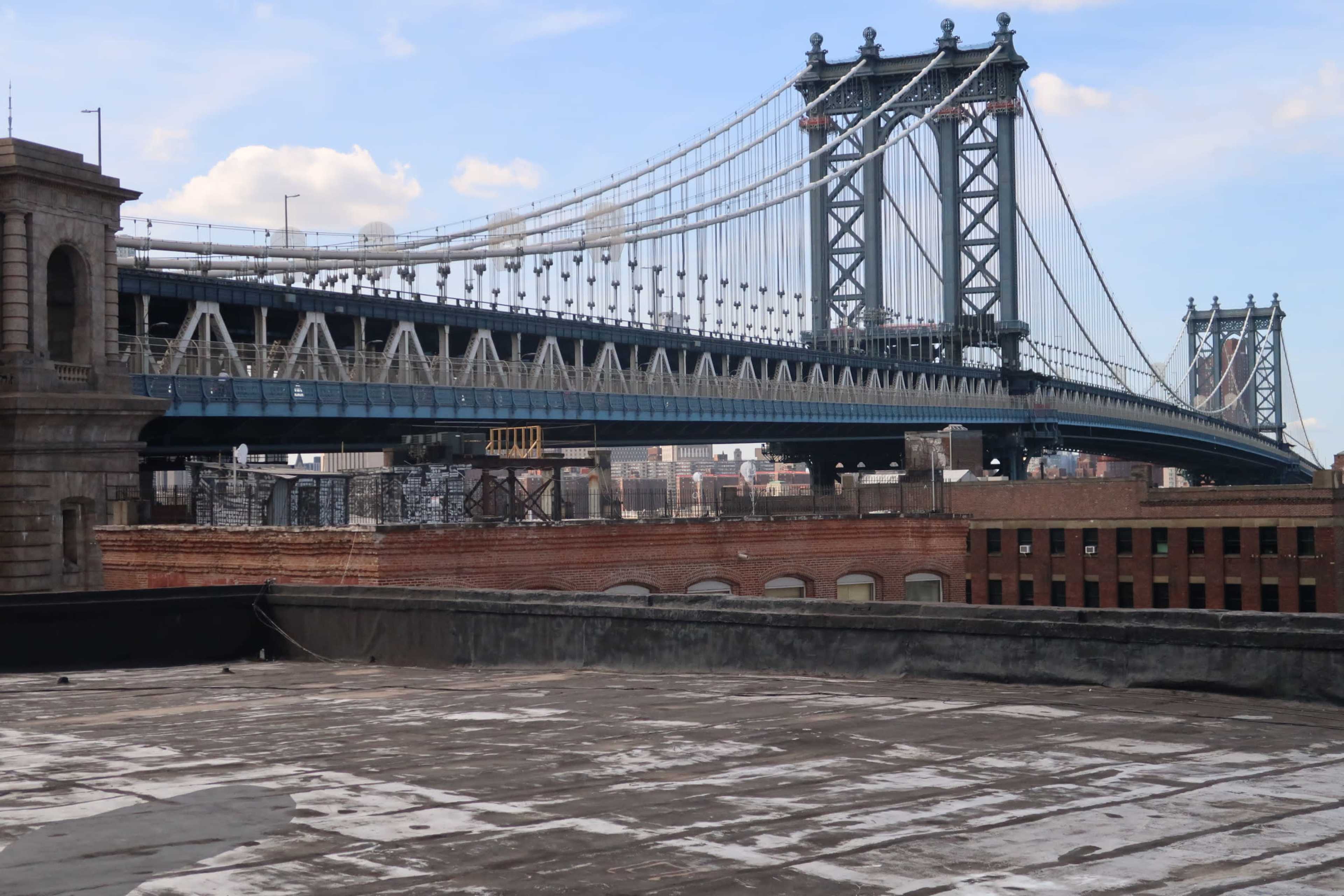 The Manhattan Bridge spanning over industrial buildings and rooftops in an urban landscape.