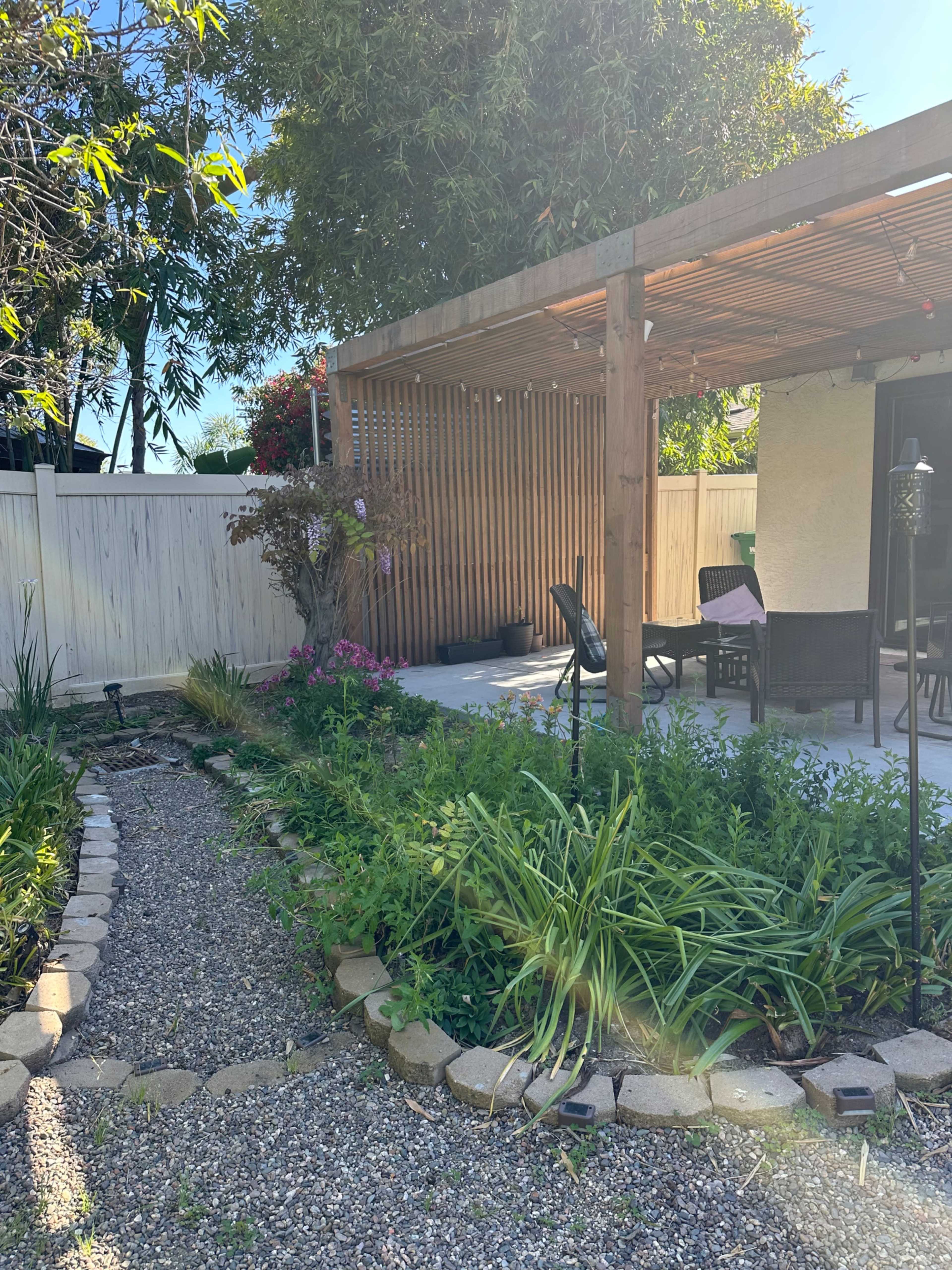 A gravel path lined with plants leads to a wooden pergola and seating area in a garden.