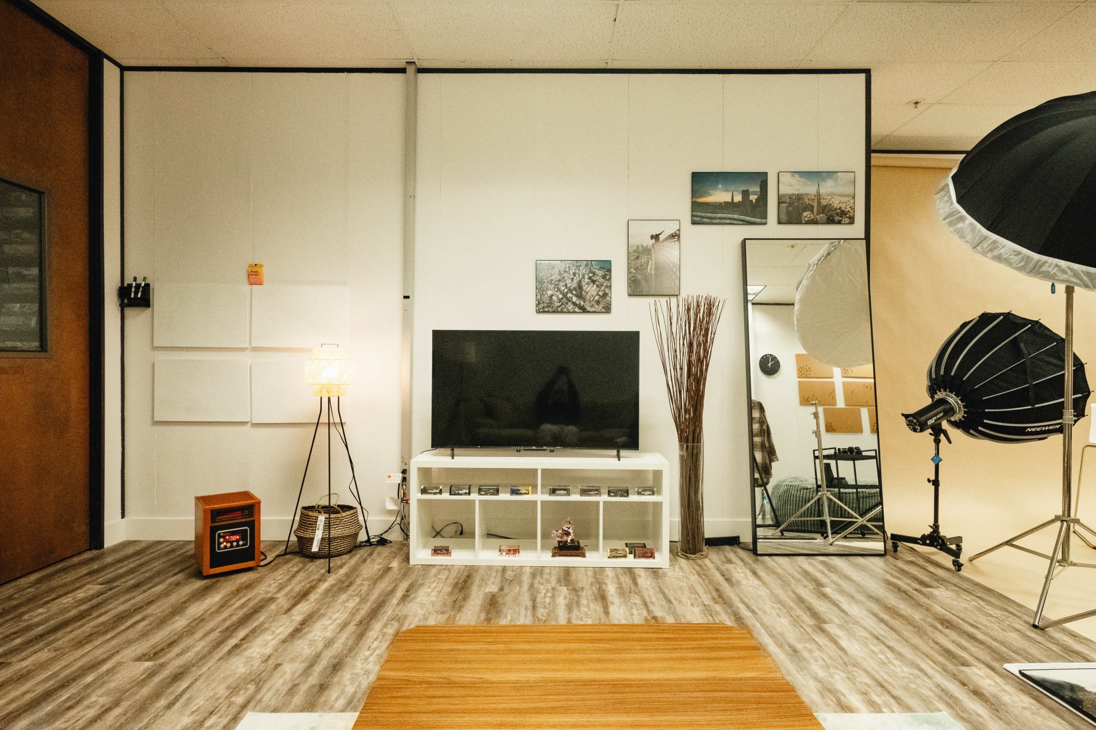 A modern studio setting with a large television on a white media console, a lamp, a mirror, and photography equipment.