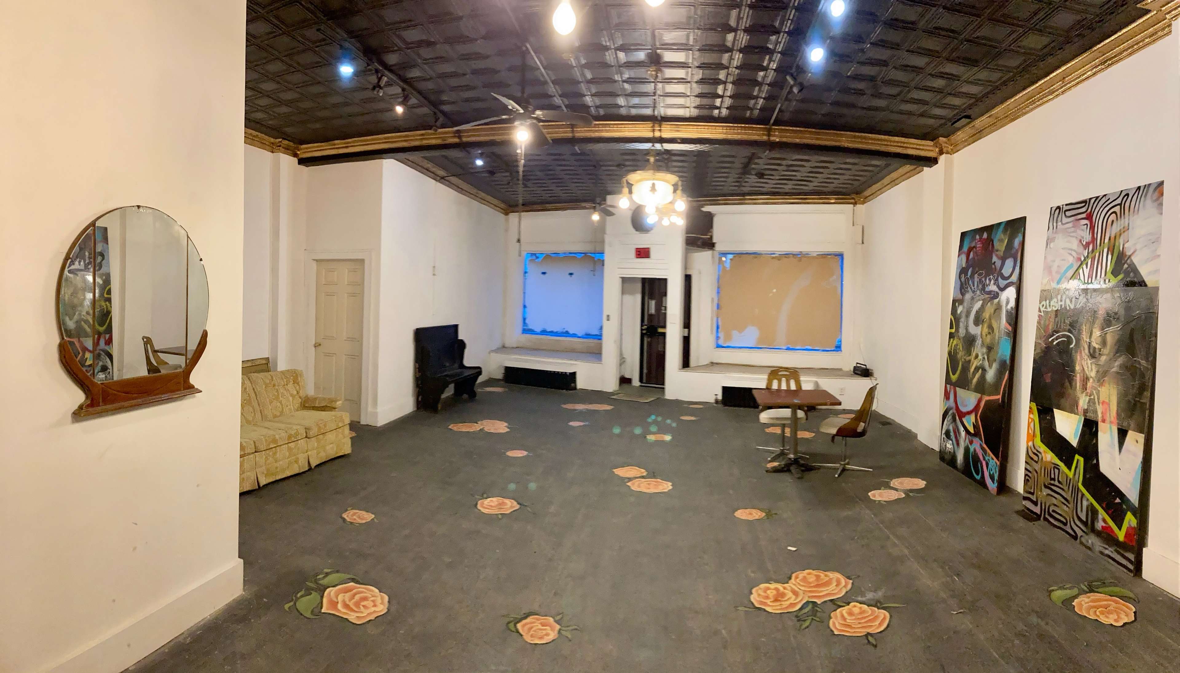 An empty room with a patterned floor and various decorations, including a sofa, a piano, and colorful wall art.