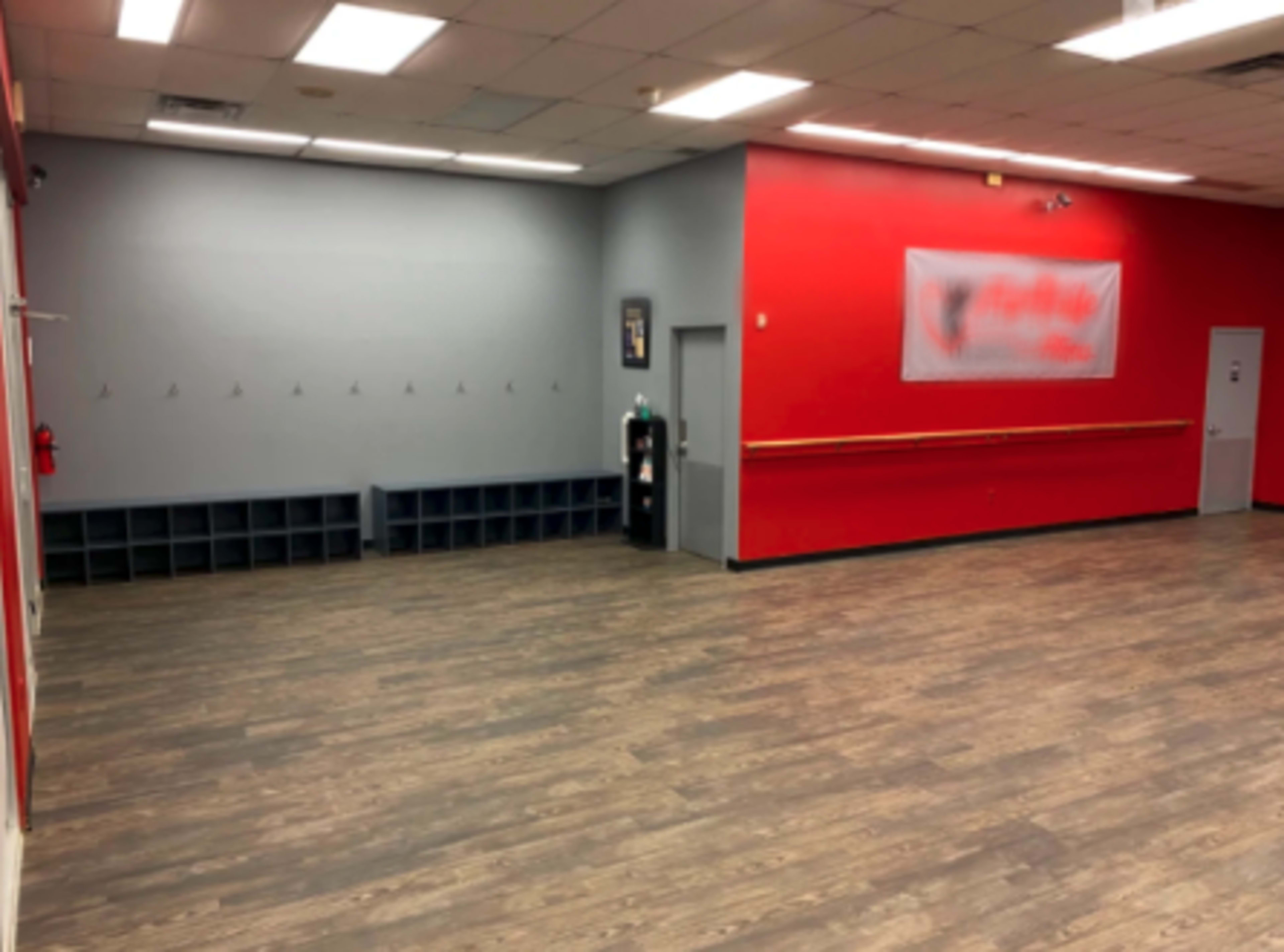 An empty indoor space with red and gray walls, wooden flooring, and a few hooks on the wall.