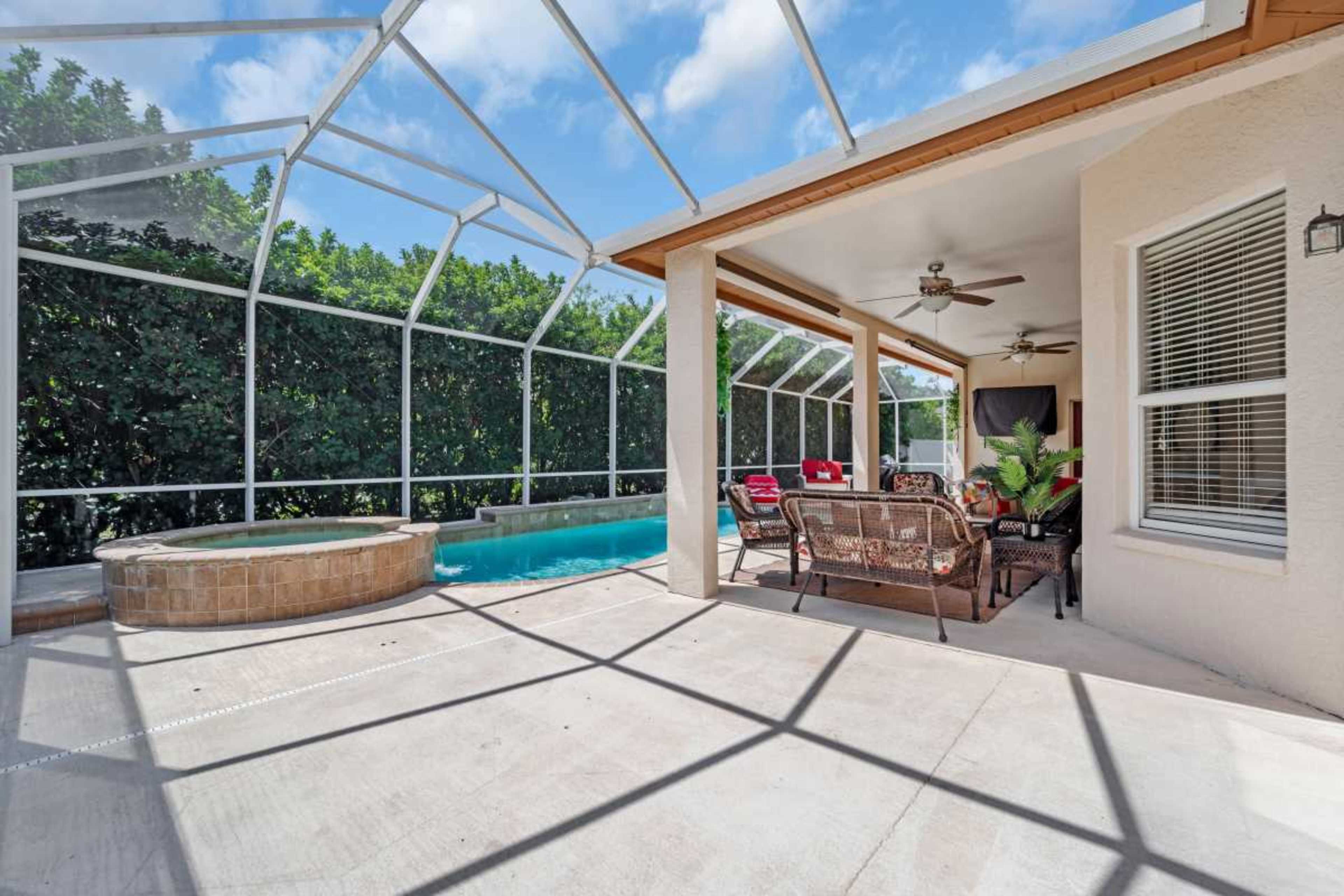 The image shows a screened patio area with a swimming pool and a hot tub, surrounded by greenery.