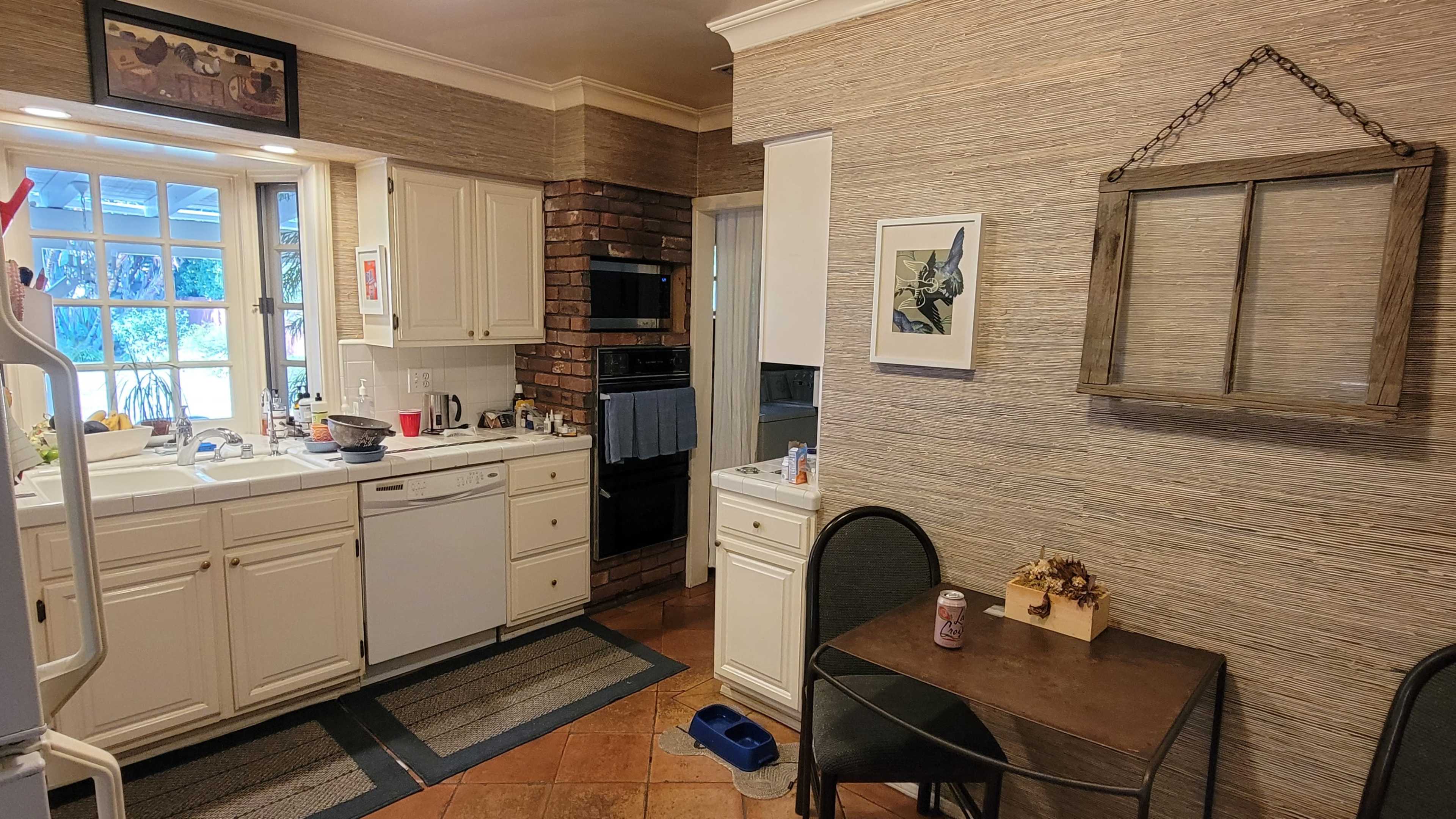 A kitchen with white cabinets, a brick accent wall, and a small dining table with two chairs.