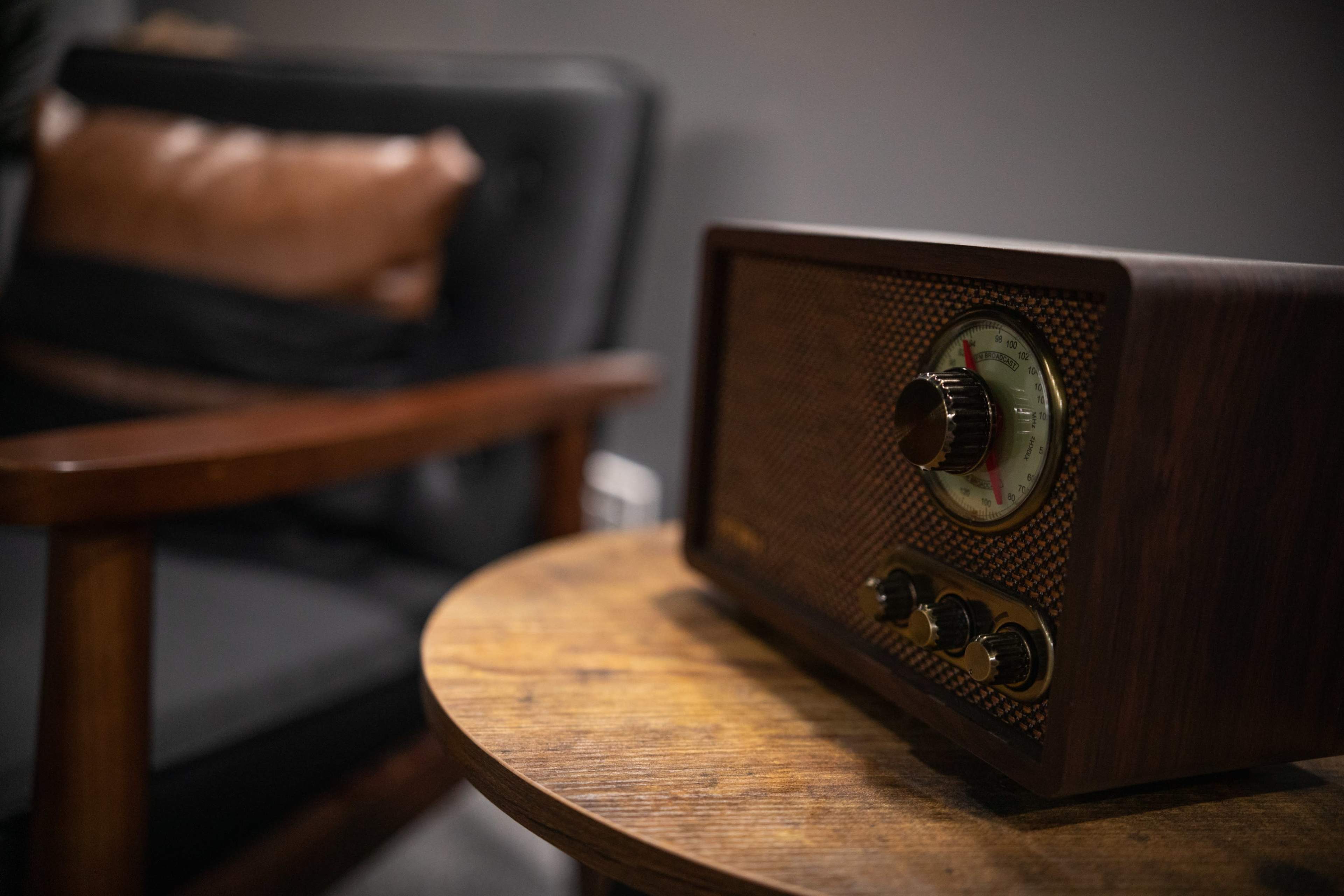 A vintage wooden radio sits on a round wooden side table beside a black armchair.