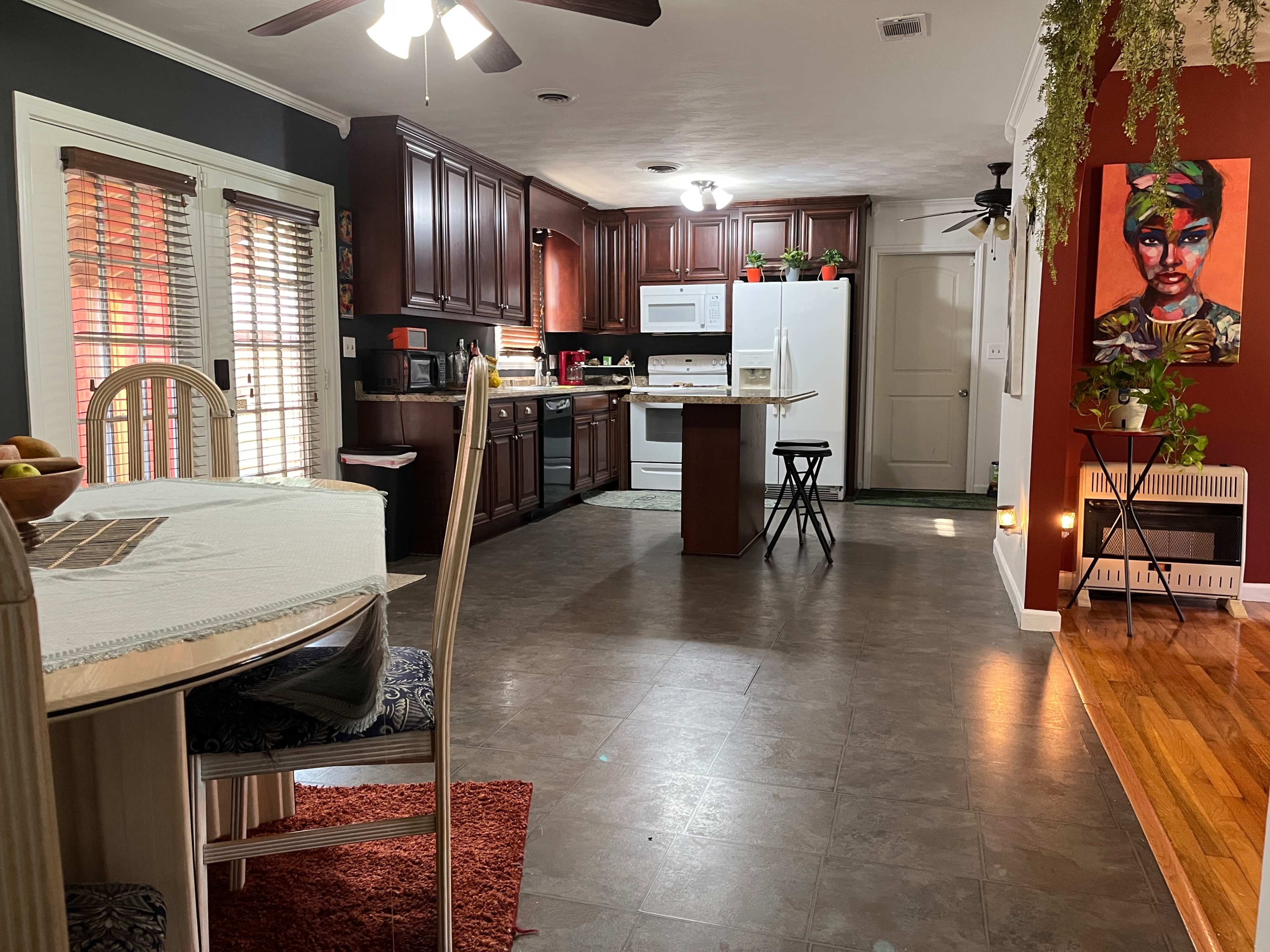 The image shows a kitchen with dark wood cabinets, white appliances, and an adjacent dining area featuring a table and chairs.