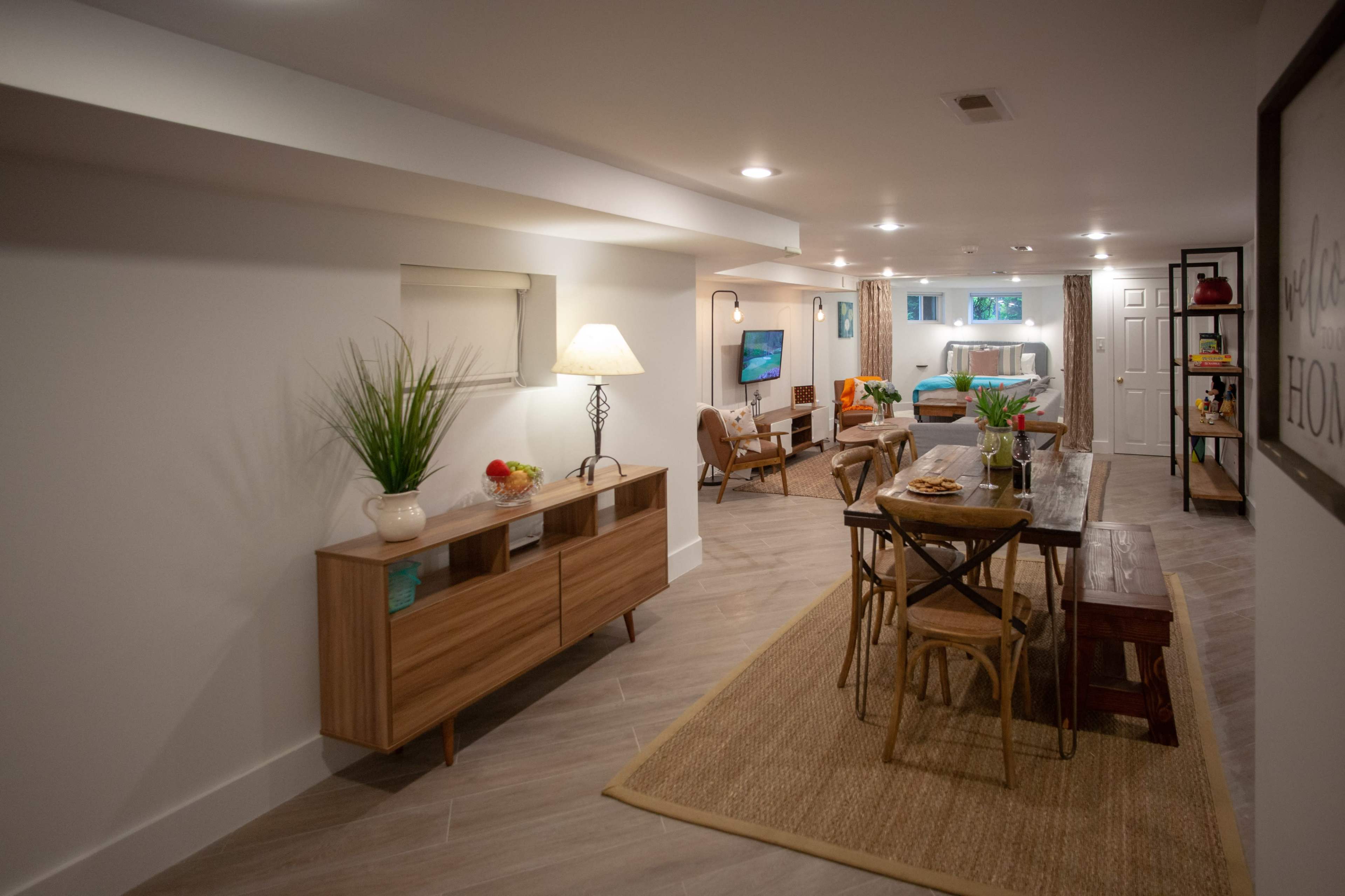 A modern, well-lit basement living space featuring a dining area, a cozy seating area, and decorative plants.