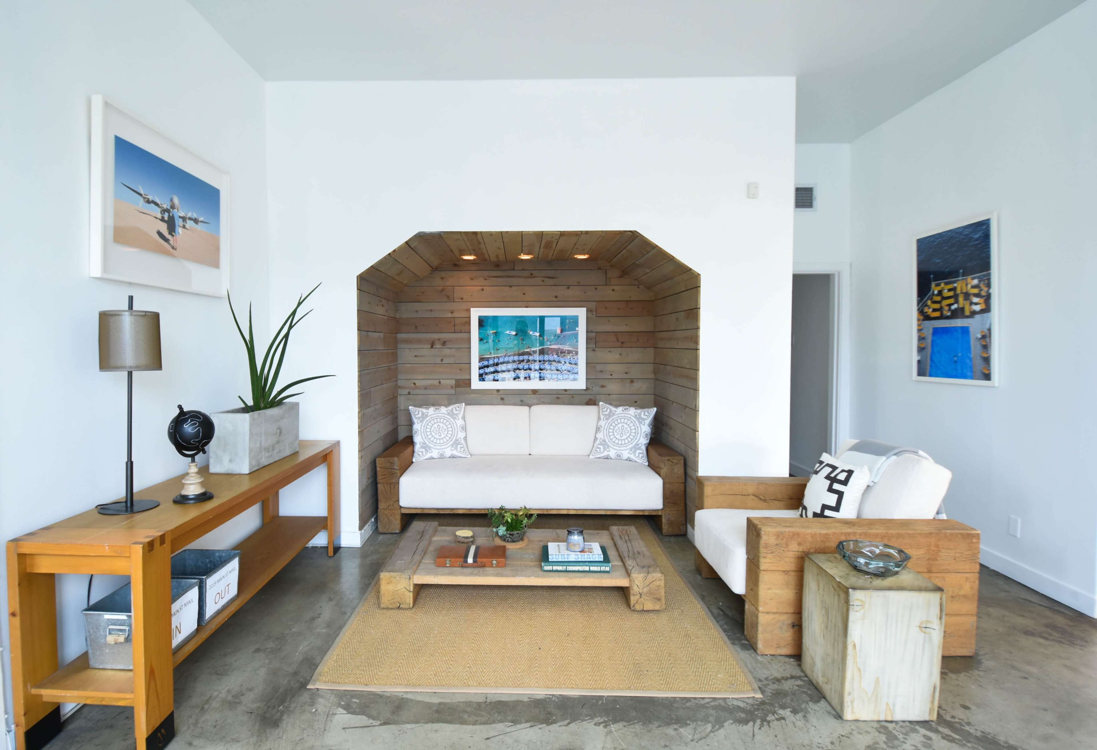 A modern living room features a wooden-paneled niche with a white sofa, two accent chairs, and a coffee table, complemented by decorative artwork and indoor plants.