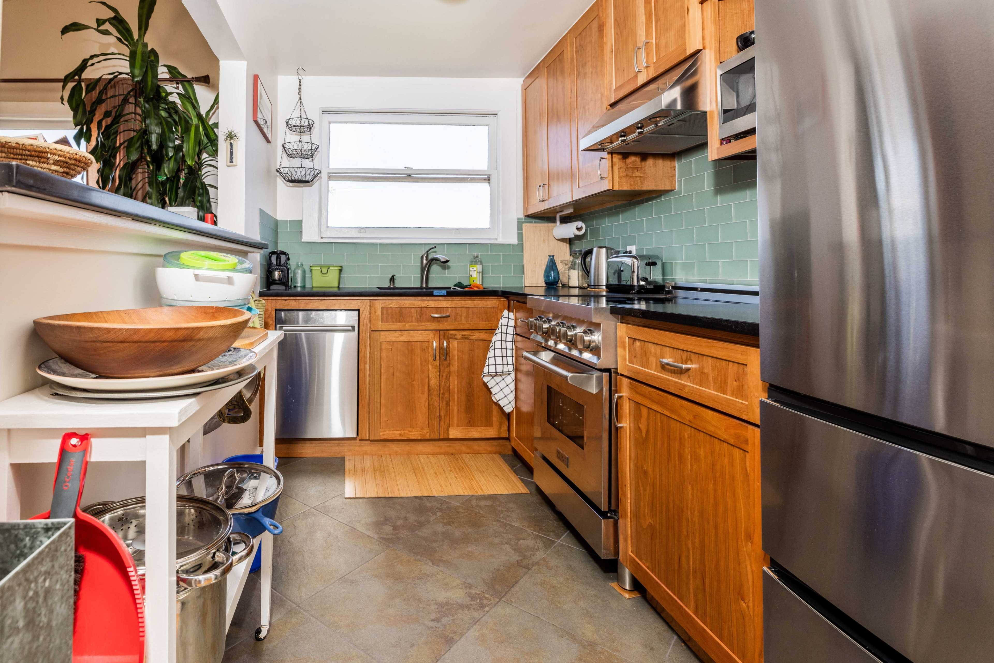 The image shows a modern kitchen with wooden cabinets, stainless steel appliances, and a countertop featuring a sink and stove.