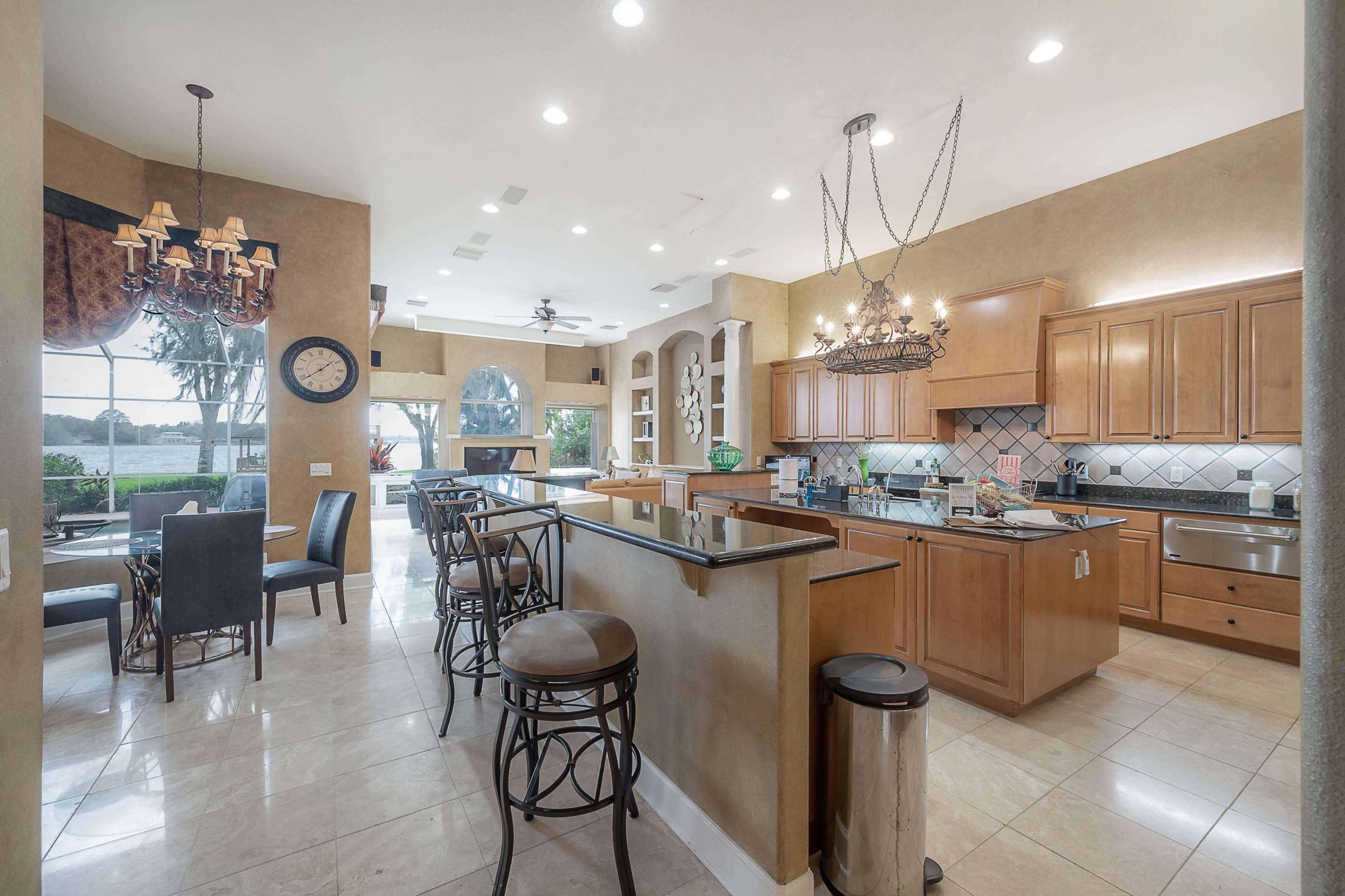 A spacious kitchen with wooden cabinetry, a central island with bar seating, and a dining area that features a round table and chairs, illuminated by natural light from large windows.