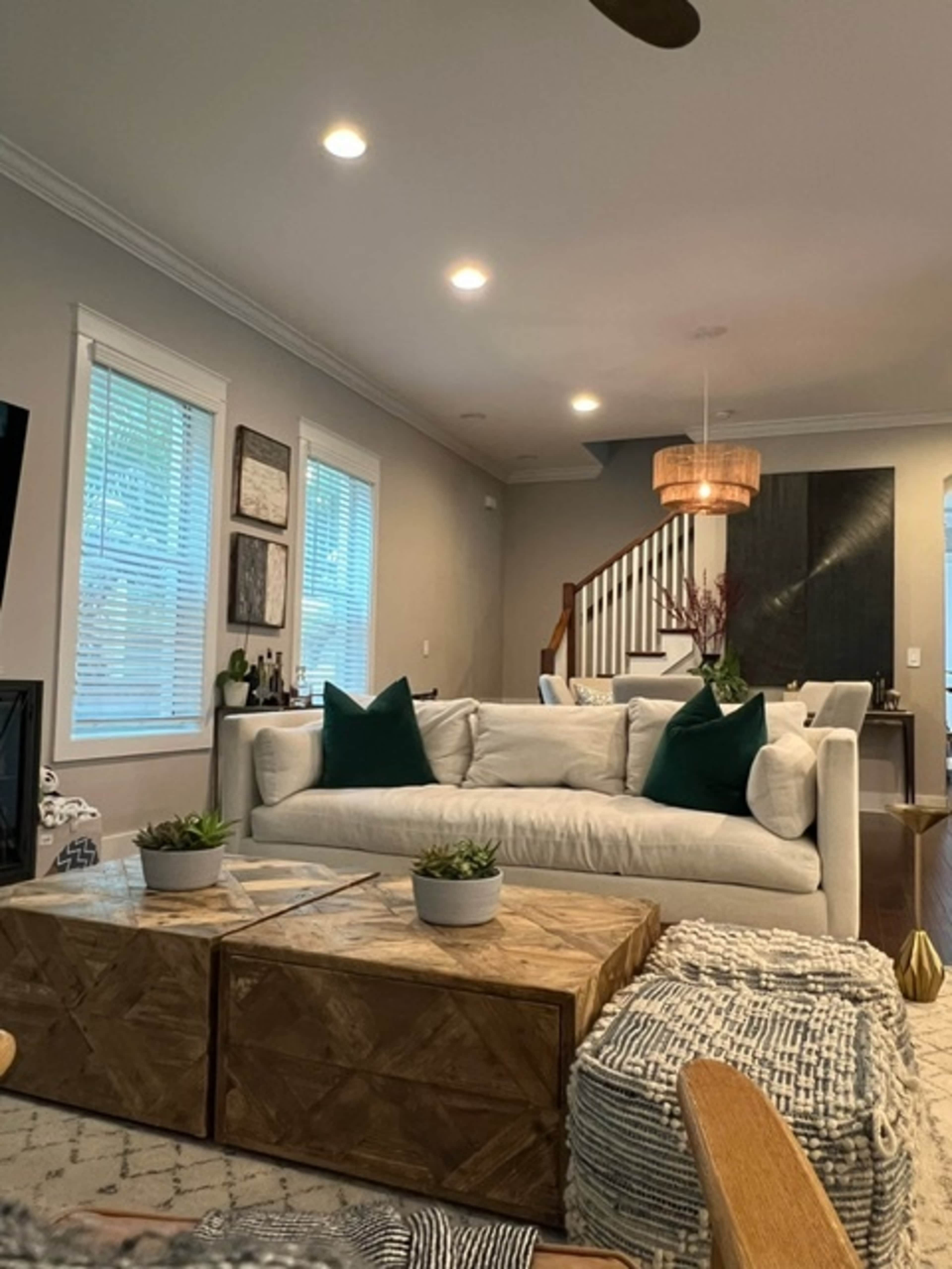 A modern living room featuring a white sofa with green pillows, a wooden coffee table, and a dining area visible in the background.