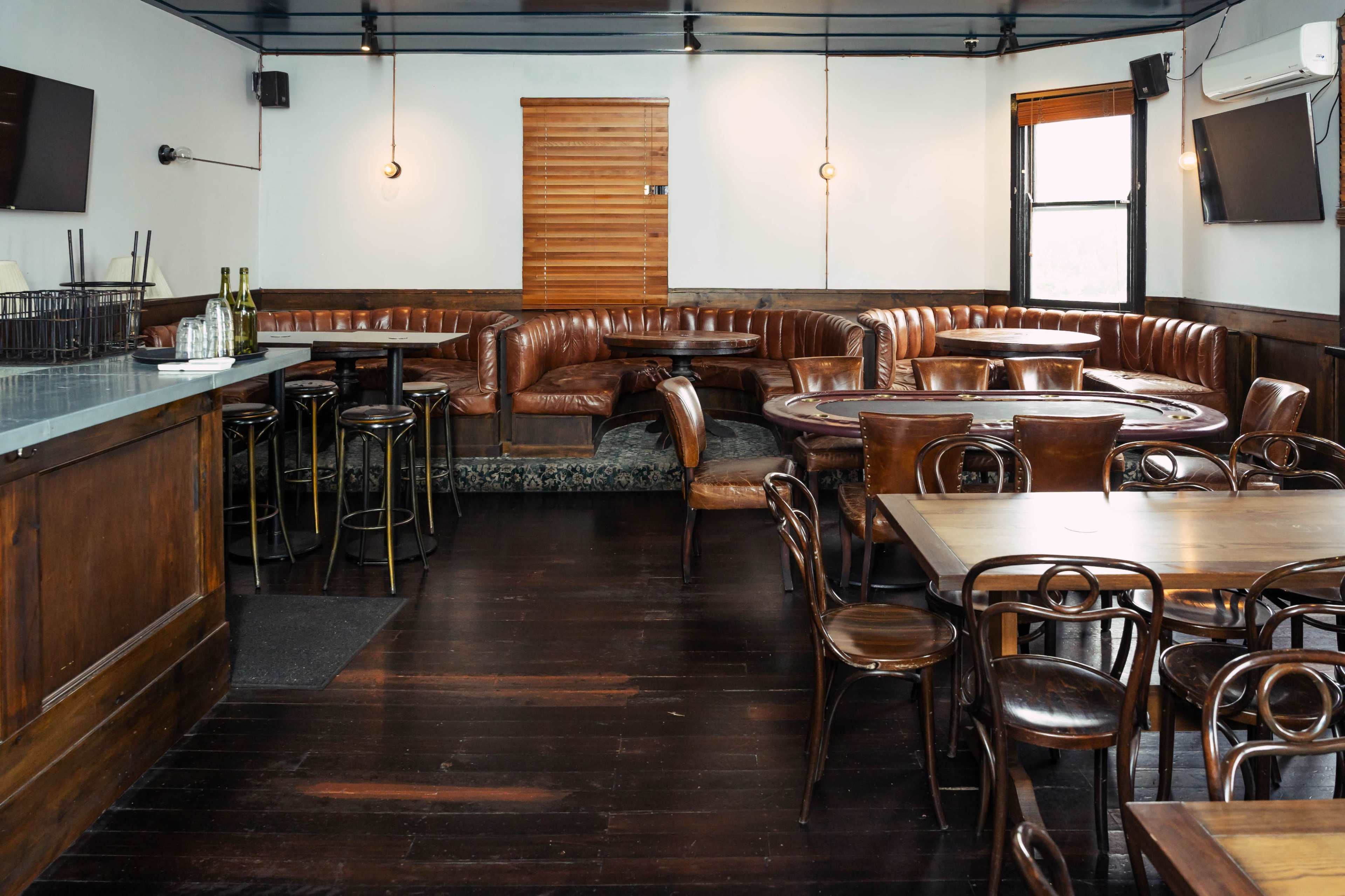 The image shows a cozy restaurant interior with wooden floors, a bar area, leather seating, and tables arranged for dining.