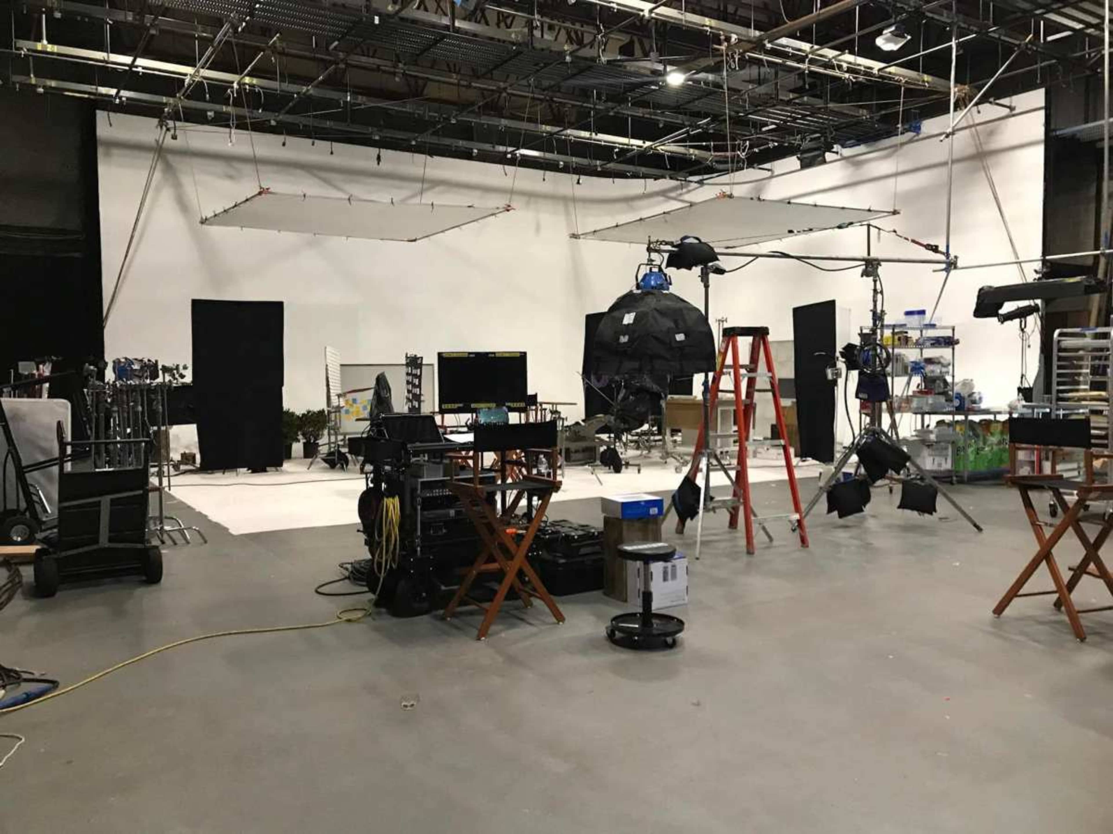 The image shows a film studio setup with various equipment, lights, and backdrops arranged for a shoot.