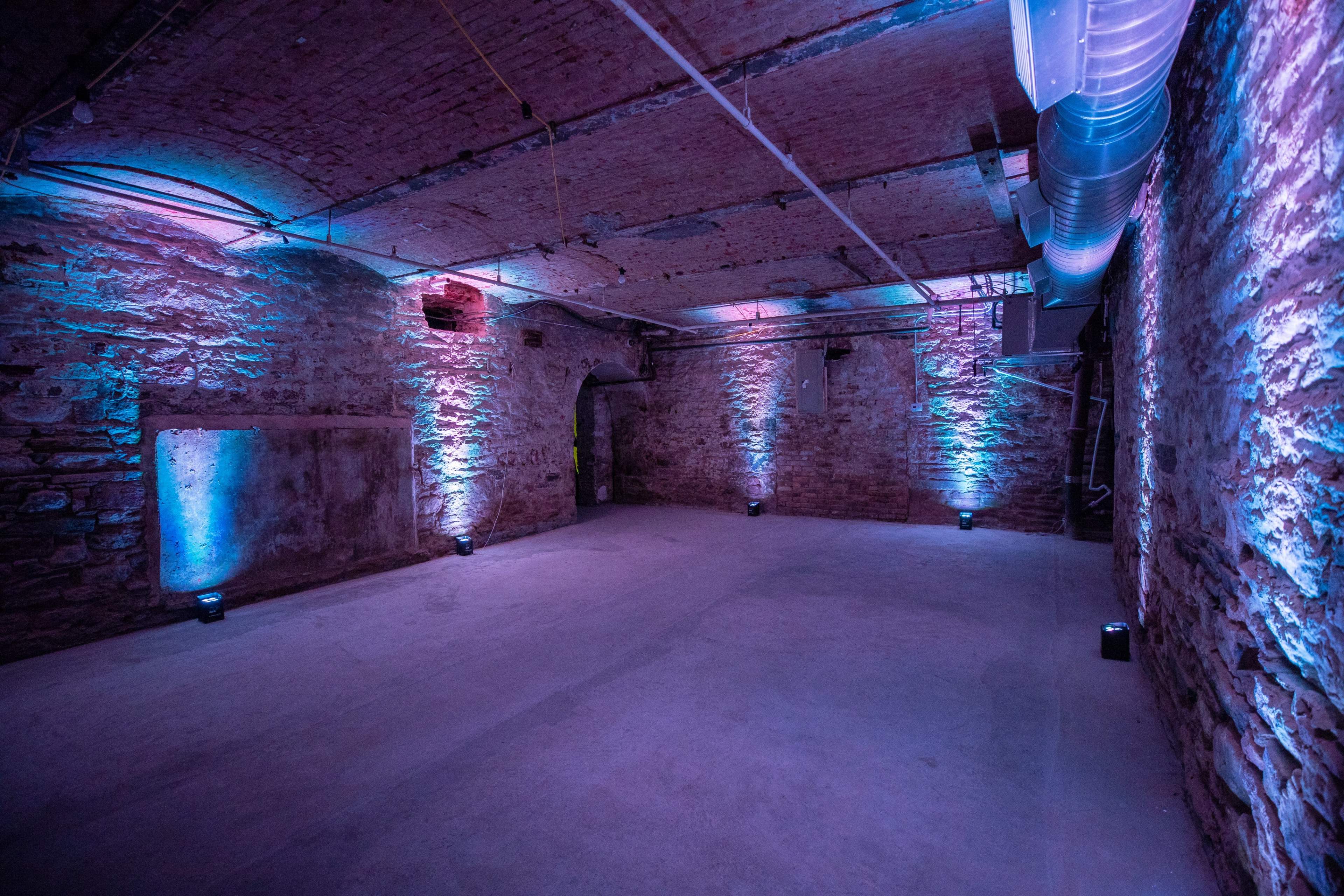 The image shows a spacious basement with exposed brick walls illuminated by blue and purple lights.