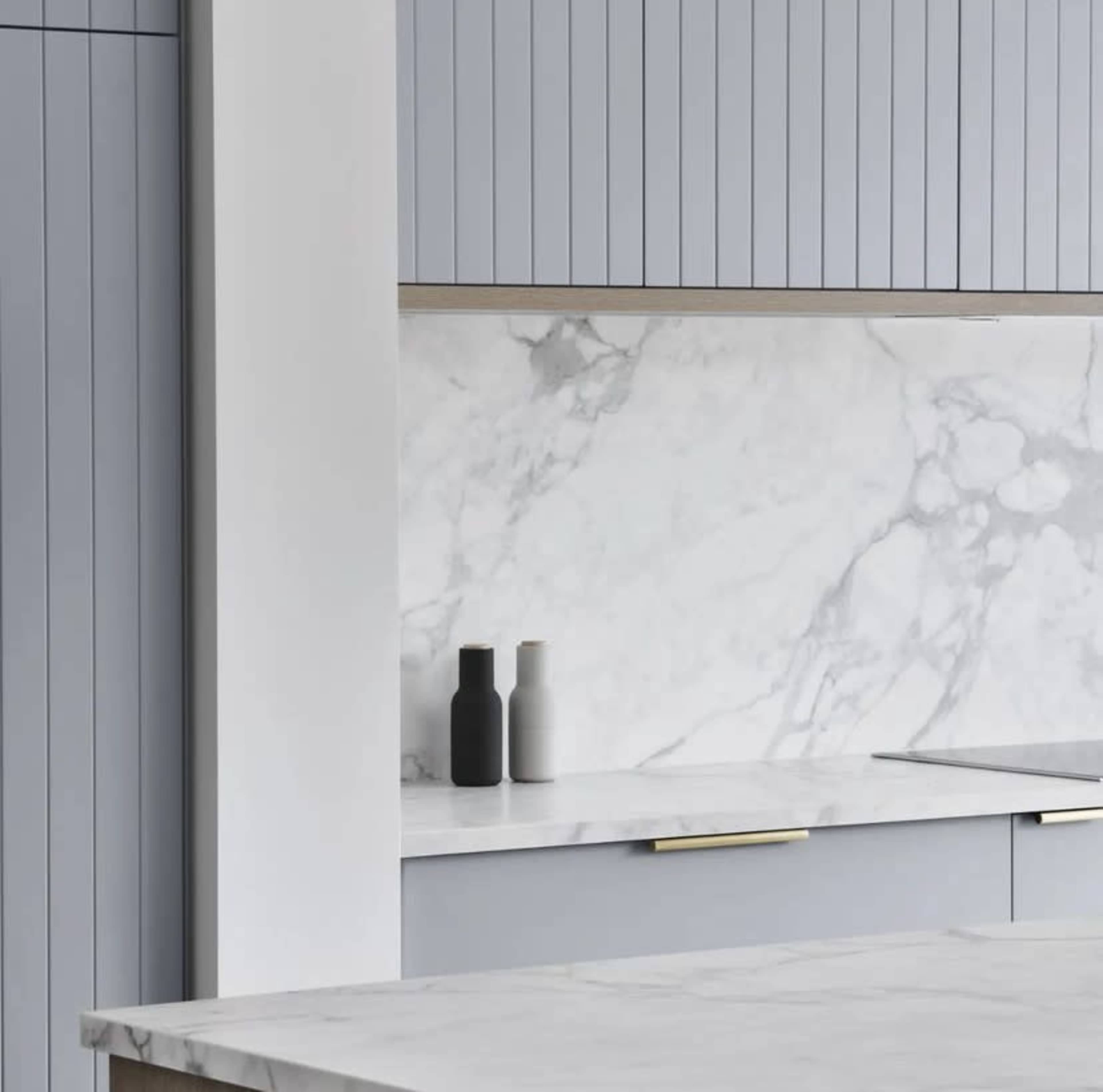 A modern kitchen features gray cabinetry, a marble backsplash, and a marble countertop with three decorative vases.