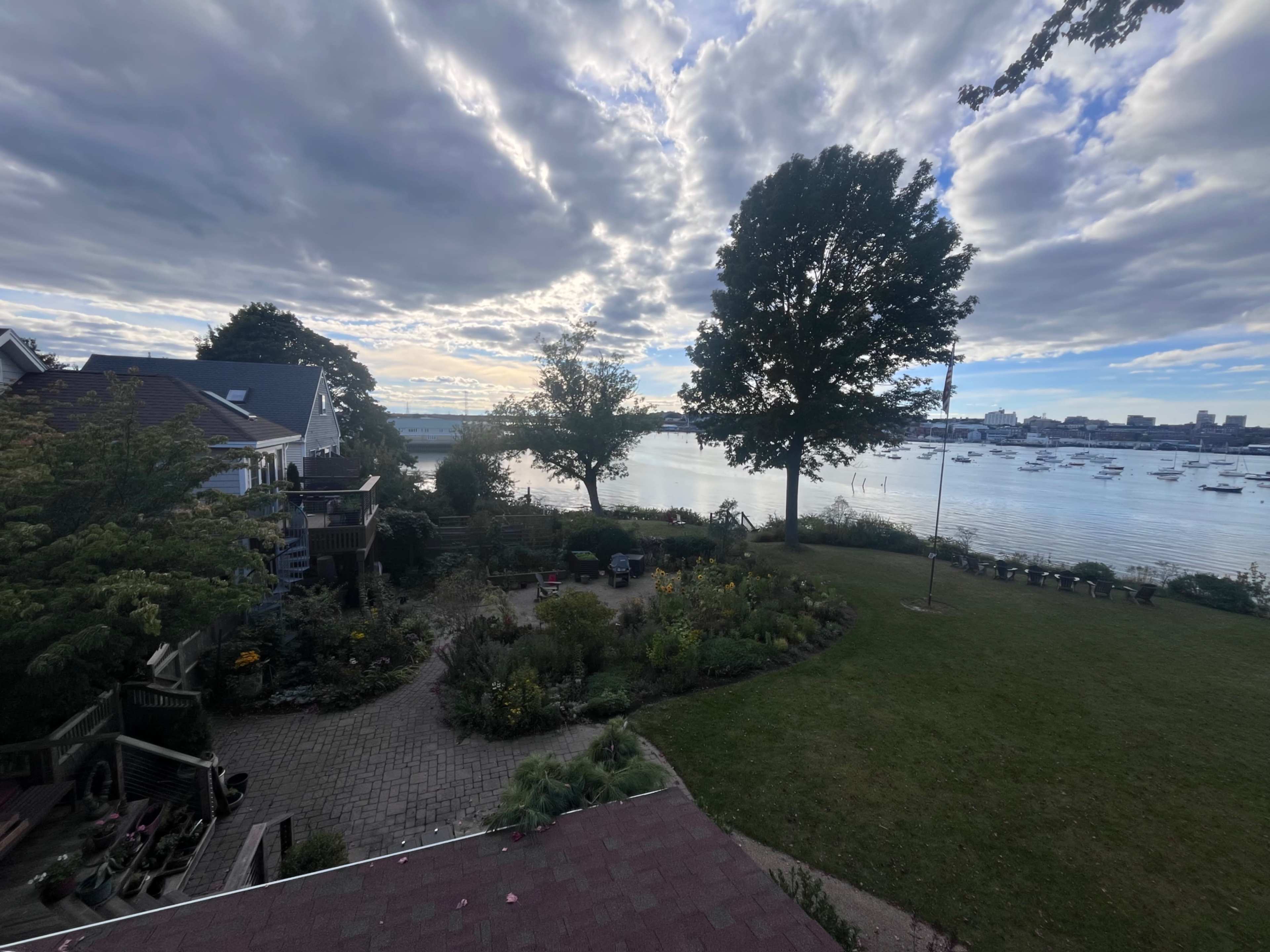 The image shows a waterfront property with a landscaped garden, a body of water, and cloudy skies above.