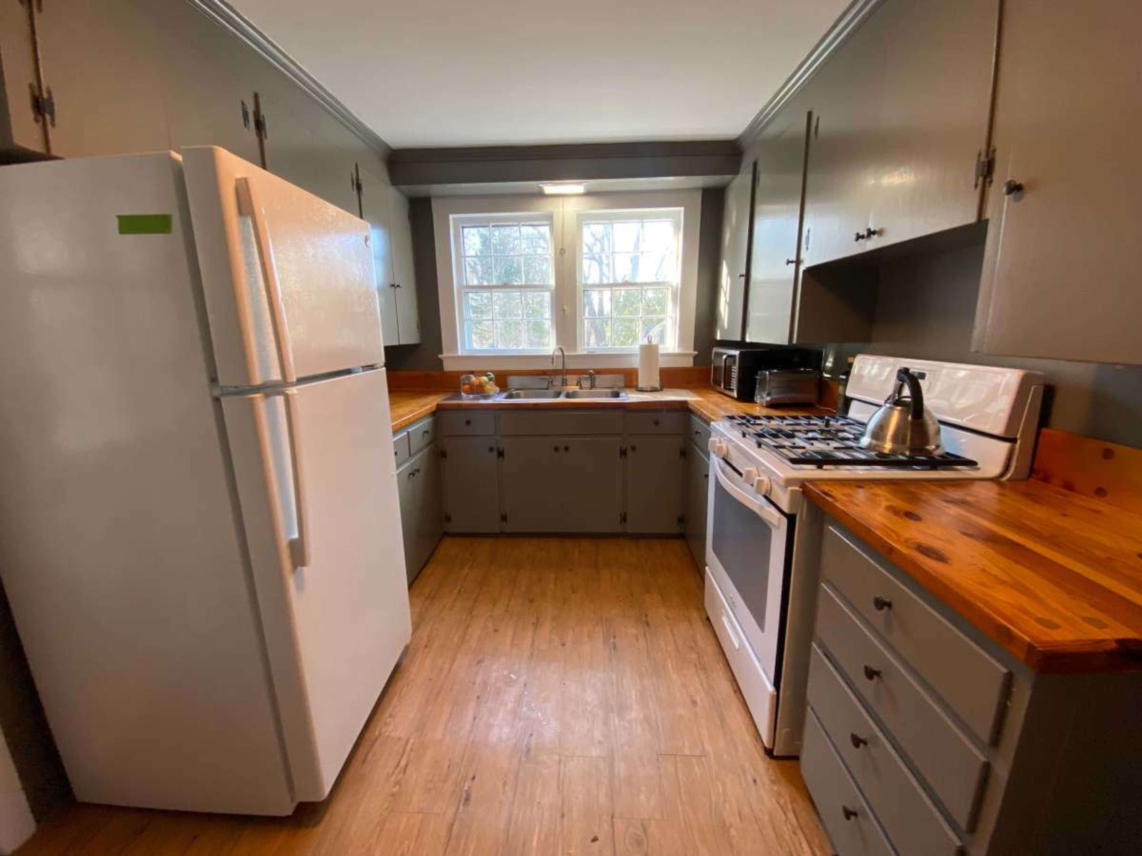 A kitchen features white appliances, wooden countertops, and gray cabinetry with a window providing natural light.
