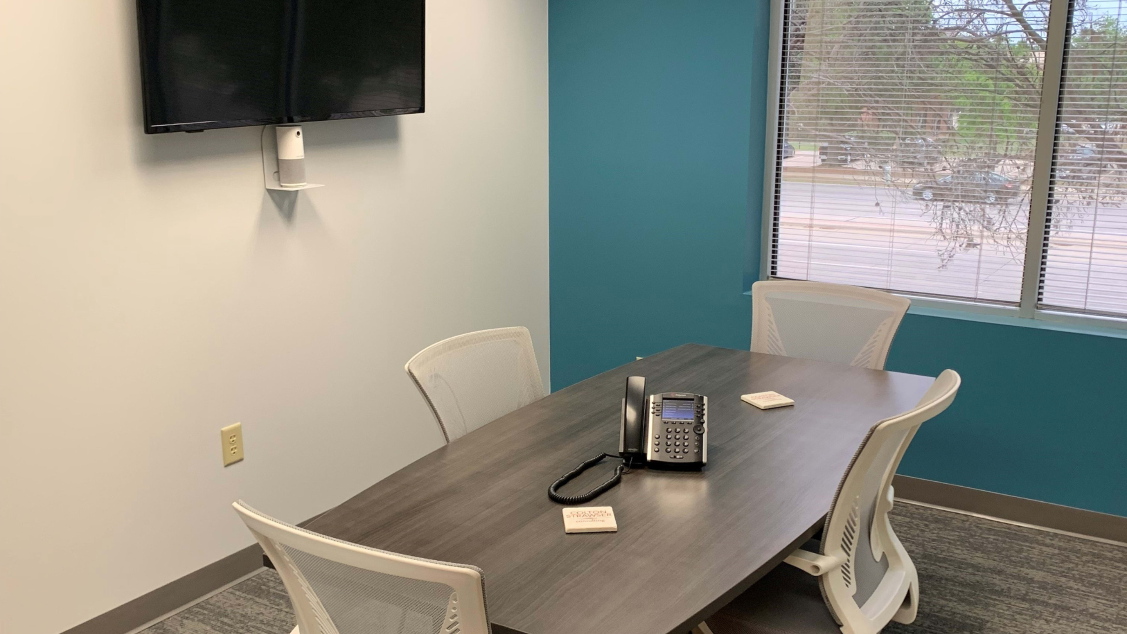 A conference room with a rectangular table, a phone on the table, and a wall-mounted television.