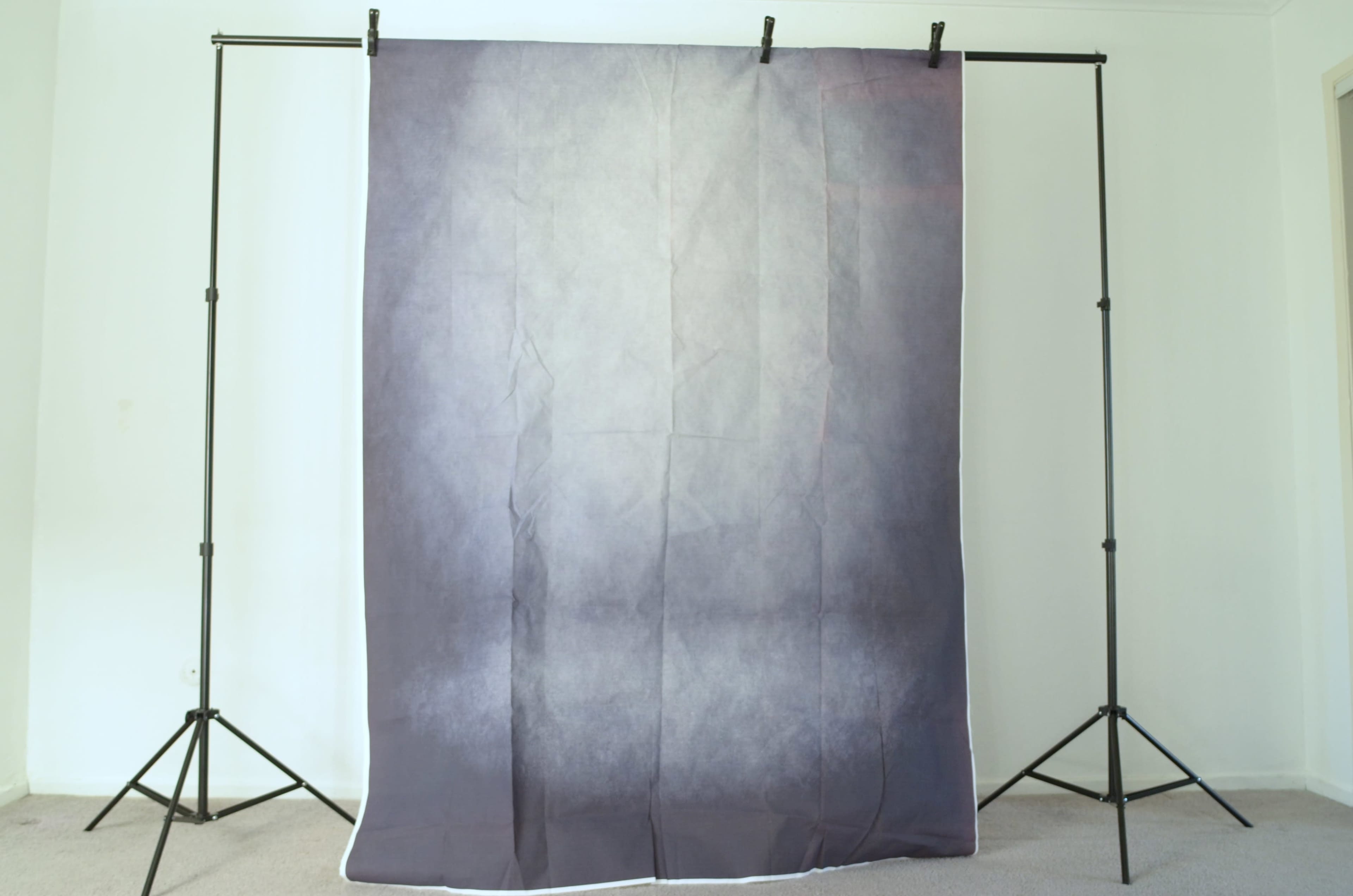 A gray fabric backdrop is suspended from a black framing stand in a room with light-colored walls and carpet.