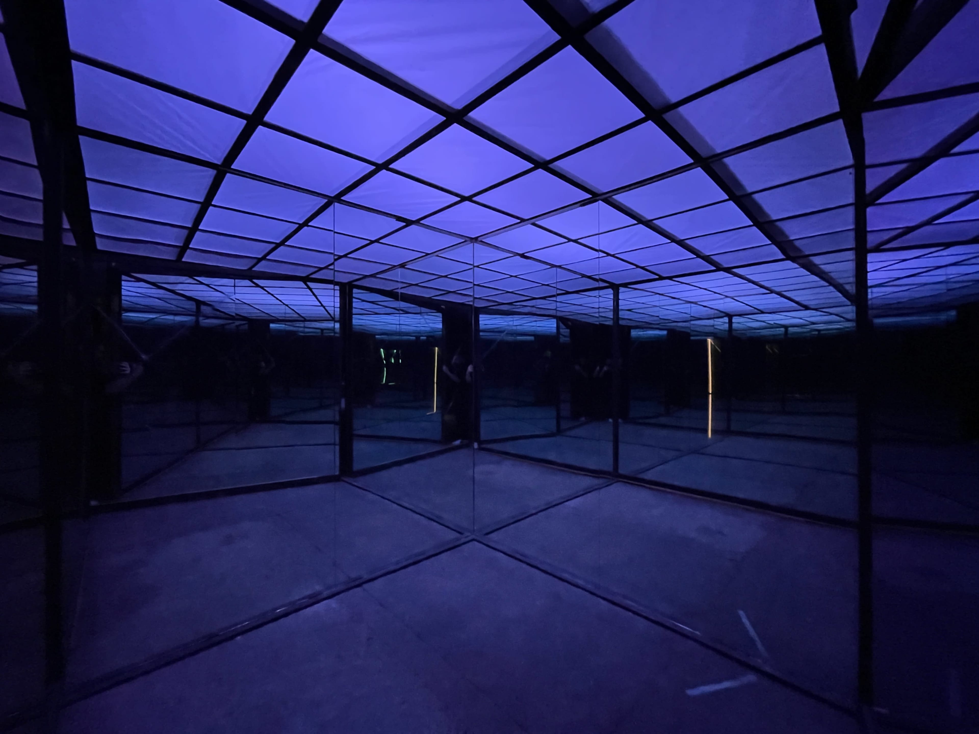A mirrored room with a grid-patterned ceiling illuminated by purple light.