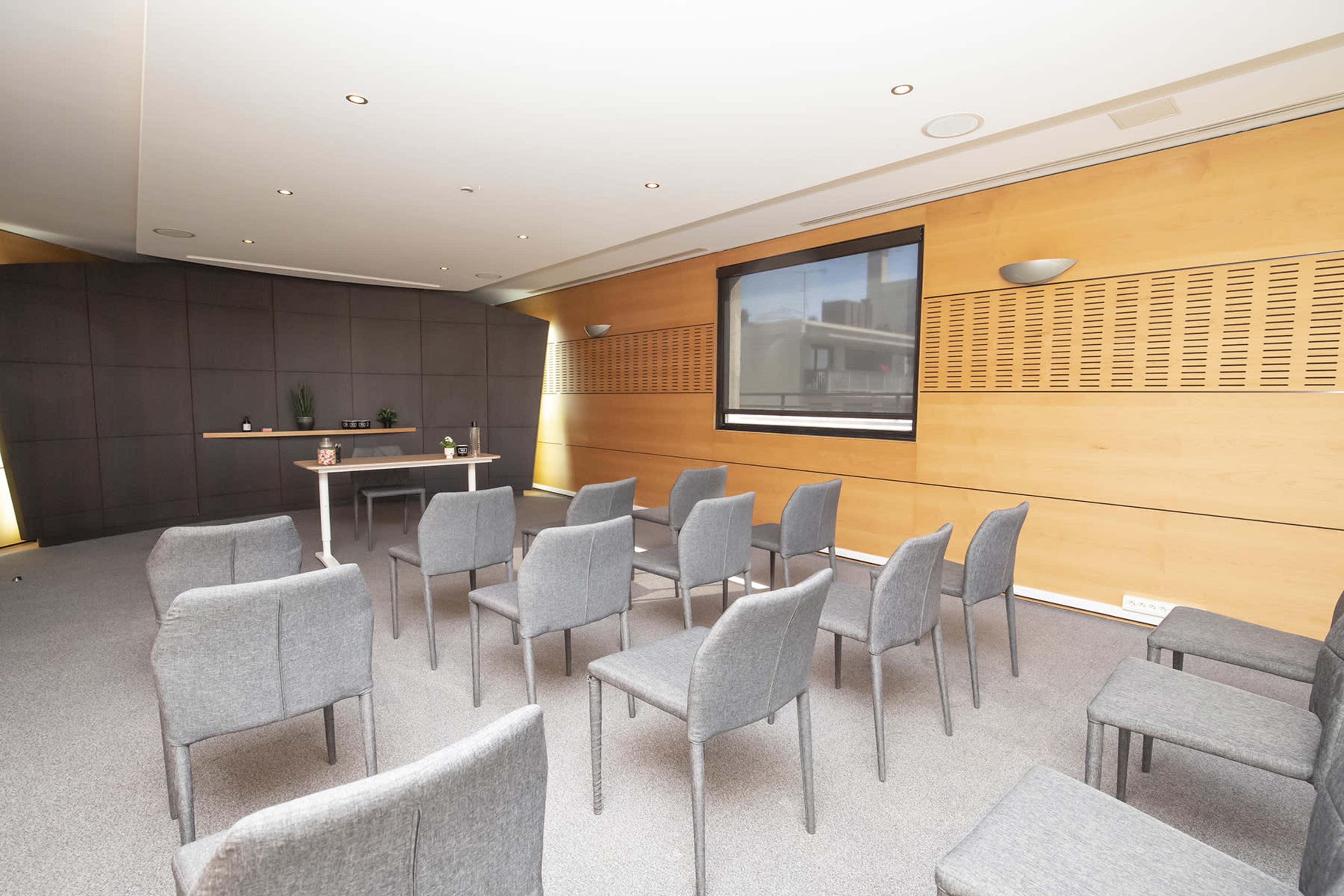 A modest conference room is set up with several gray chairs facing a central table and a large screen on the wall.