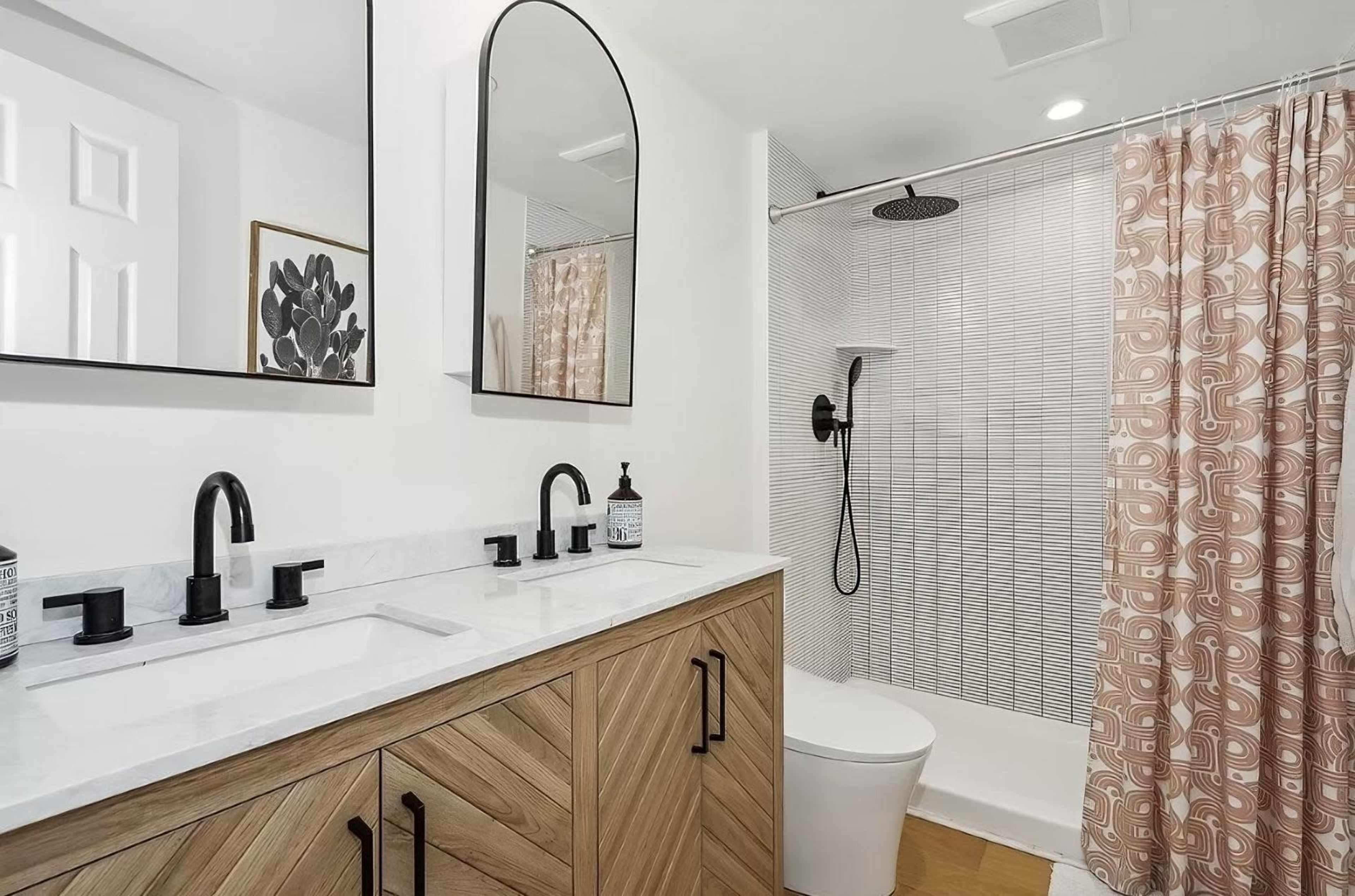The bathroom features a double vanity with a wooden base, round mirrors above each sink, and a shower area separated by a patterned curtain.