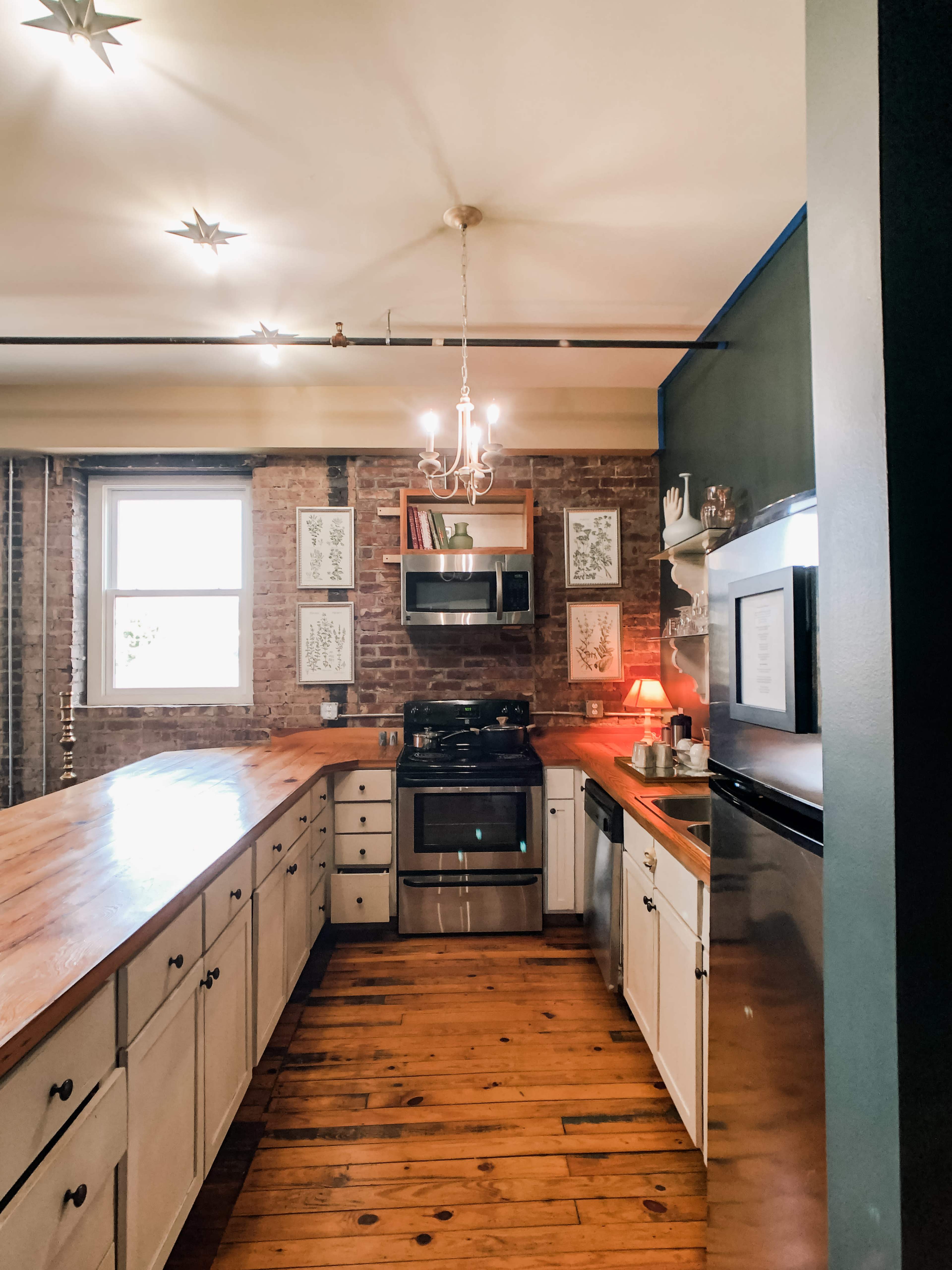 The kitchen features a wooden countertop, brick walls, and modern appliances, with decorative artwork displayed on the walls.