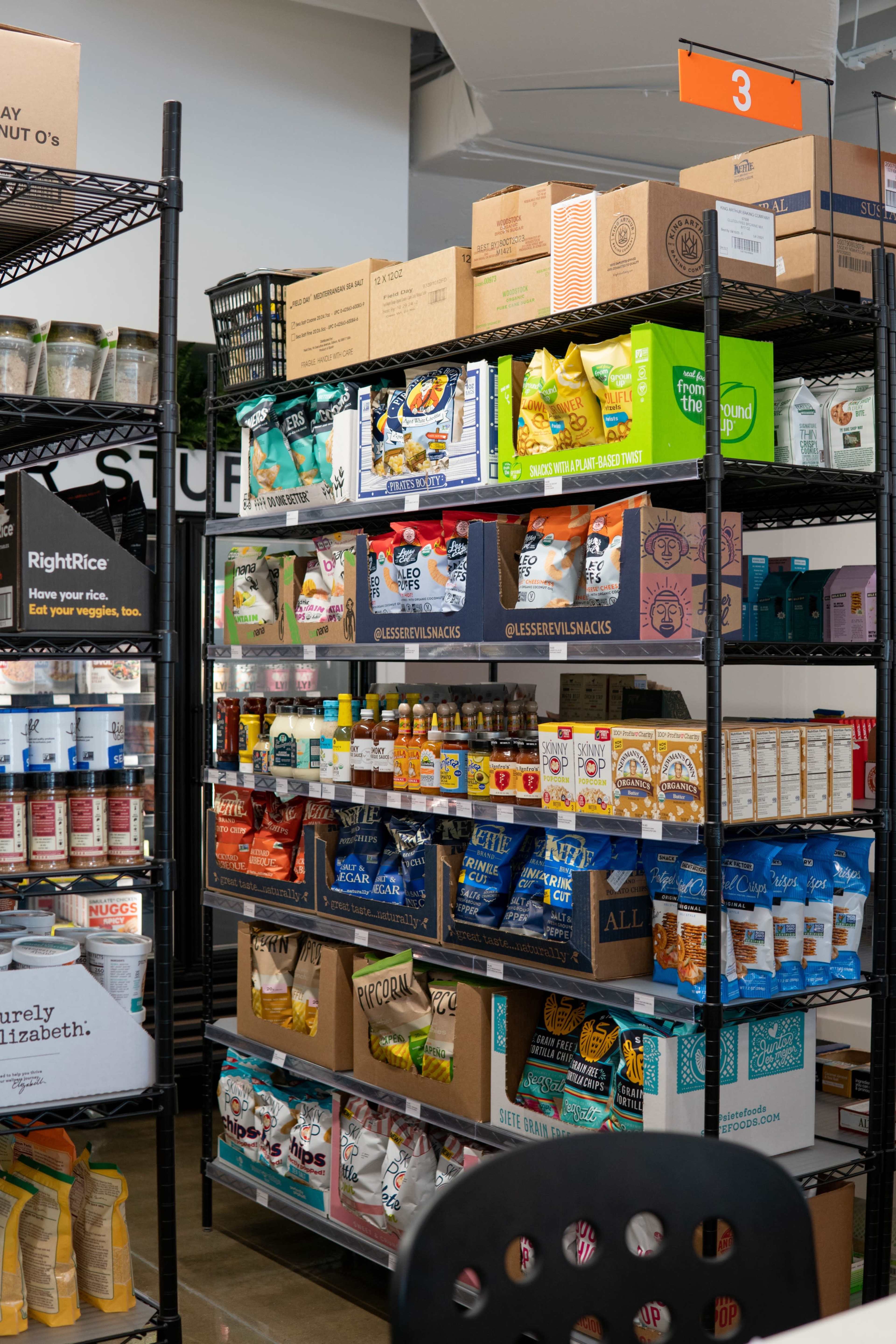 A metal shelving unit displays various snack products and beverages in a retail environment.