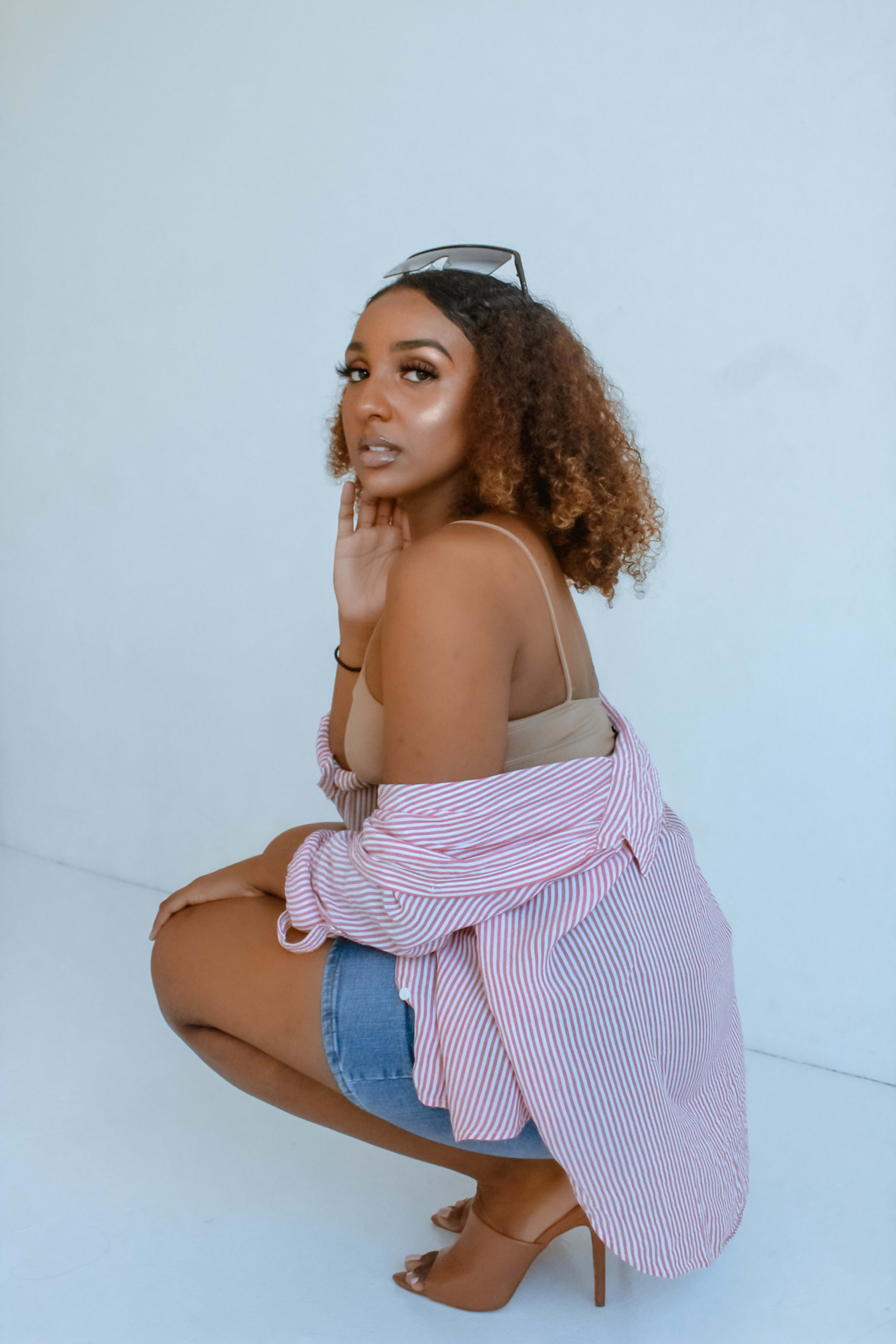 A woman posing for a photo shoot while squatting on the ground with her hand under her chin.