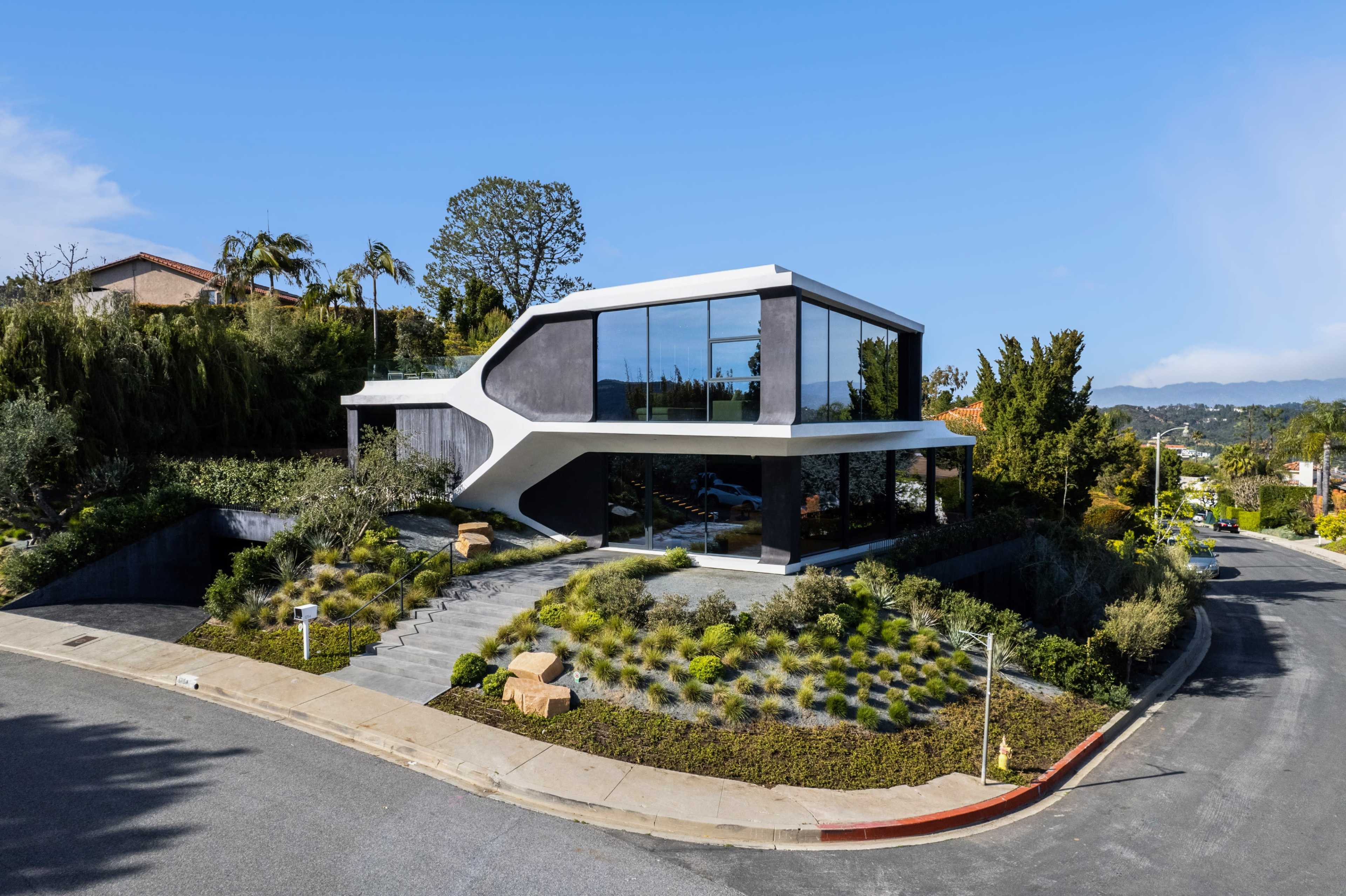 A modern house with a unique design featuring large glass windows and a landscaped yard sits at the corner of a residential street.