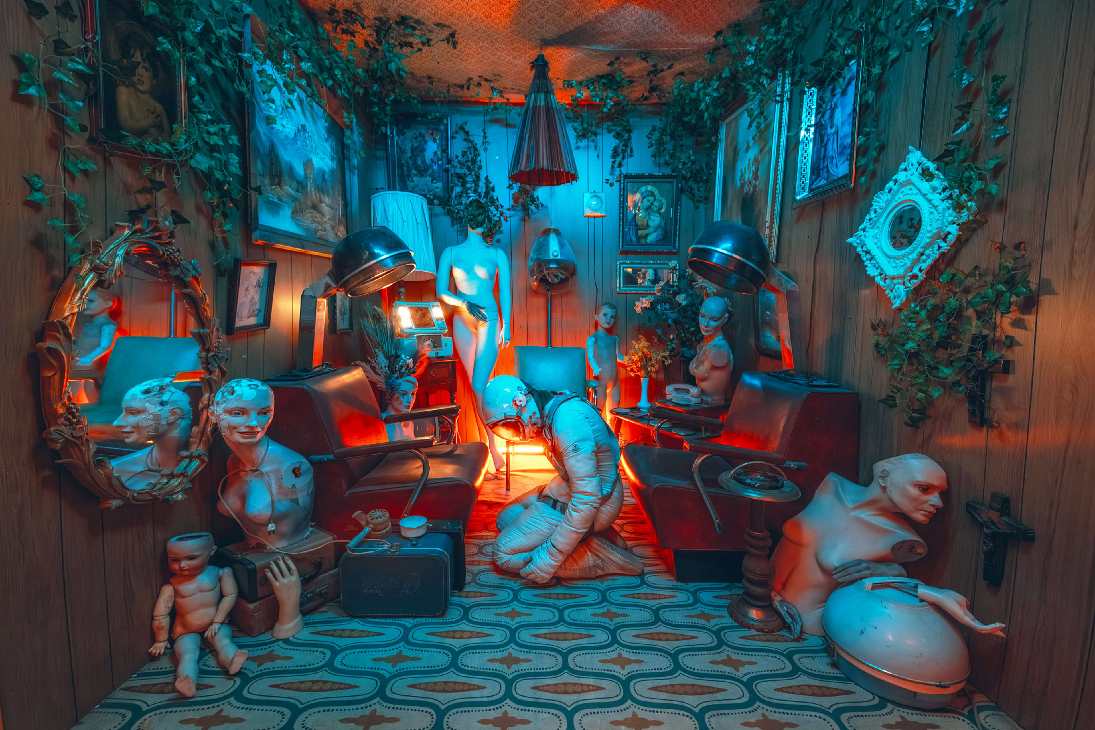 The image depicts an eerie, dimly lit room filled with various mannequins and sculptures, featuring vintage hair salon chairs and wall art, all surrounded by greenery.