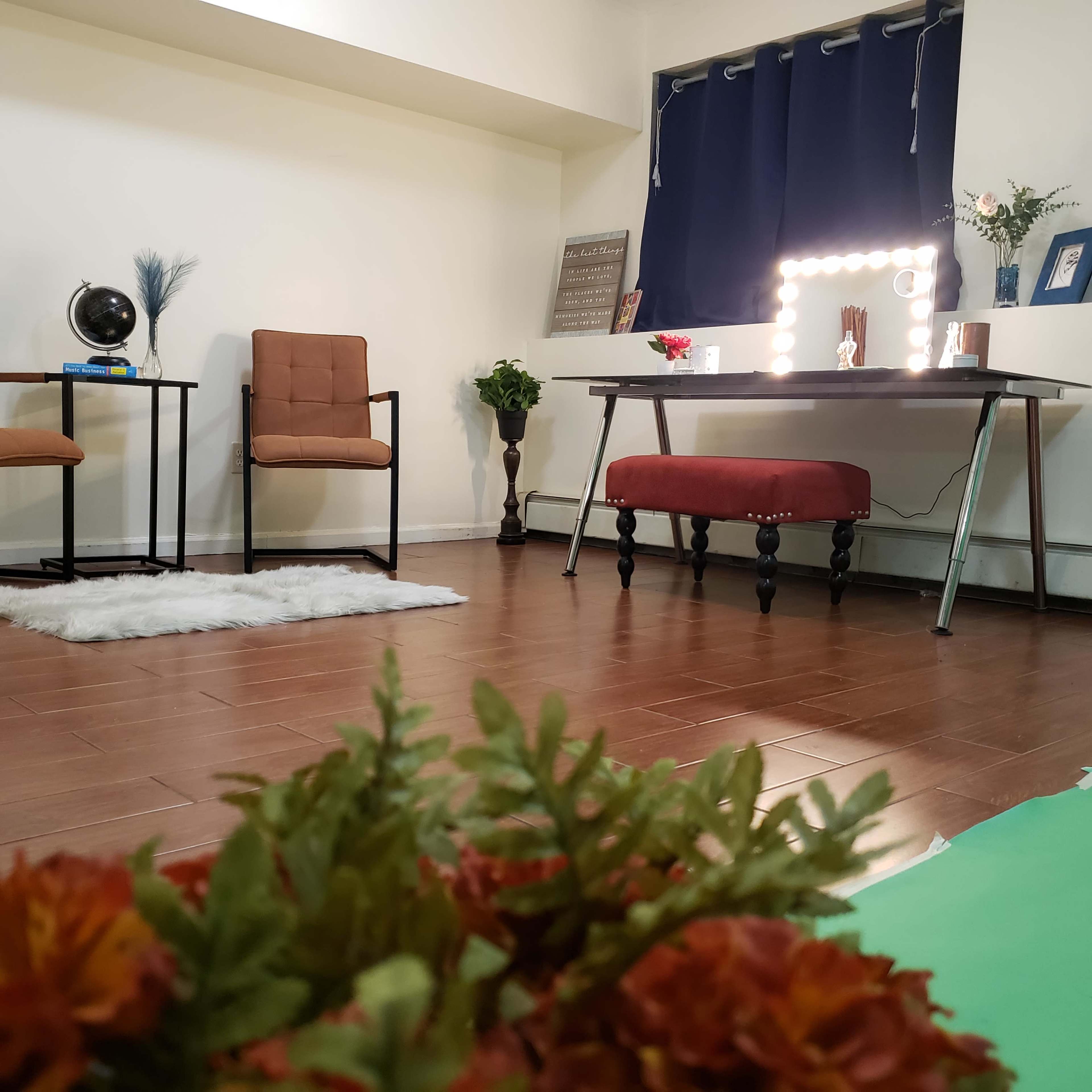 A tidy interior space featuring two chairs, a mirror with lights on a desk, and decorative plants.