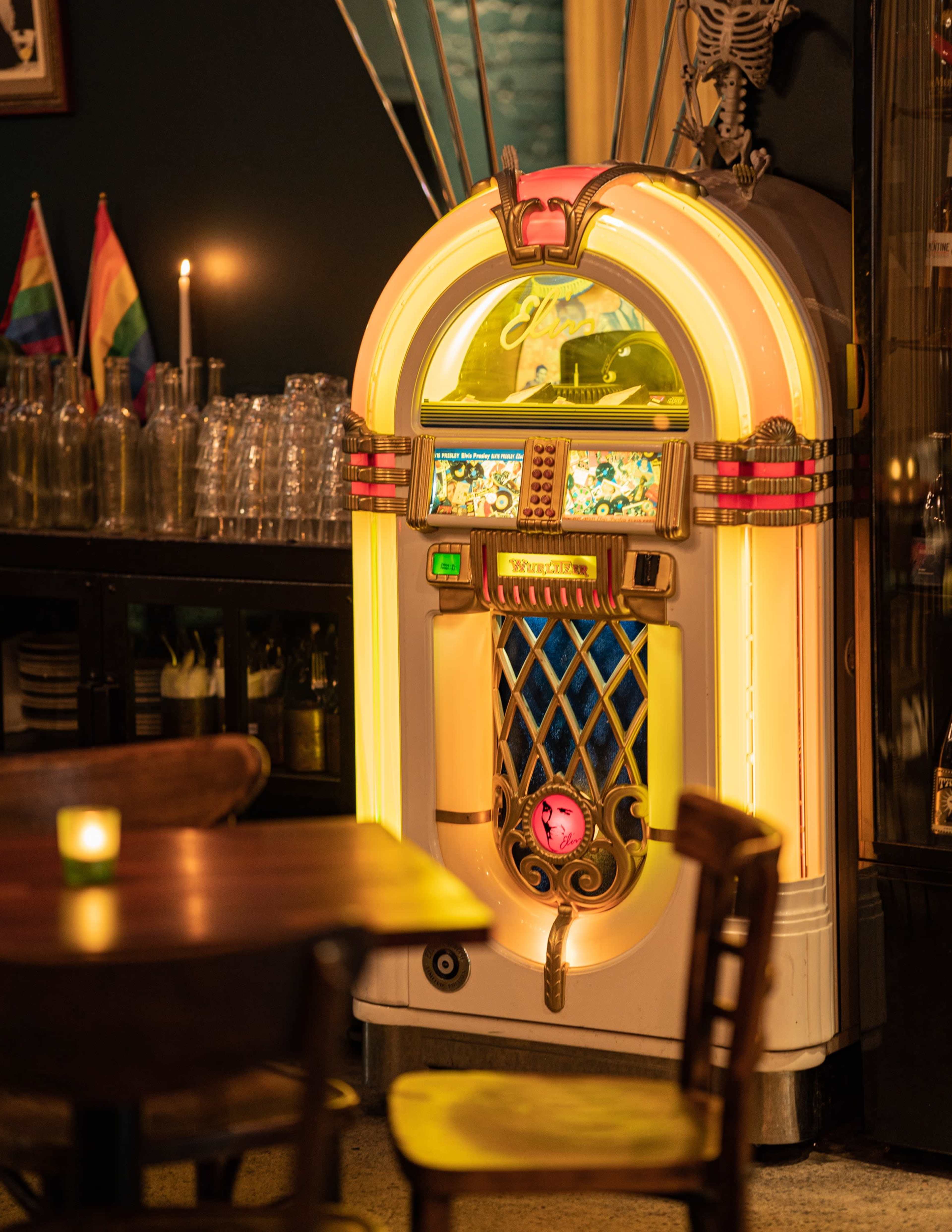 A vintage jukebox stands illuminated against a dark wall in a cozy bar setting.