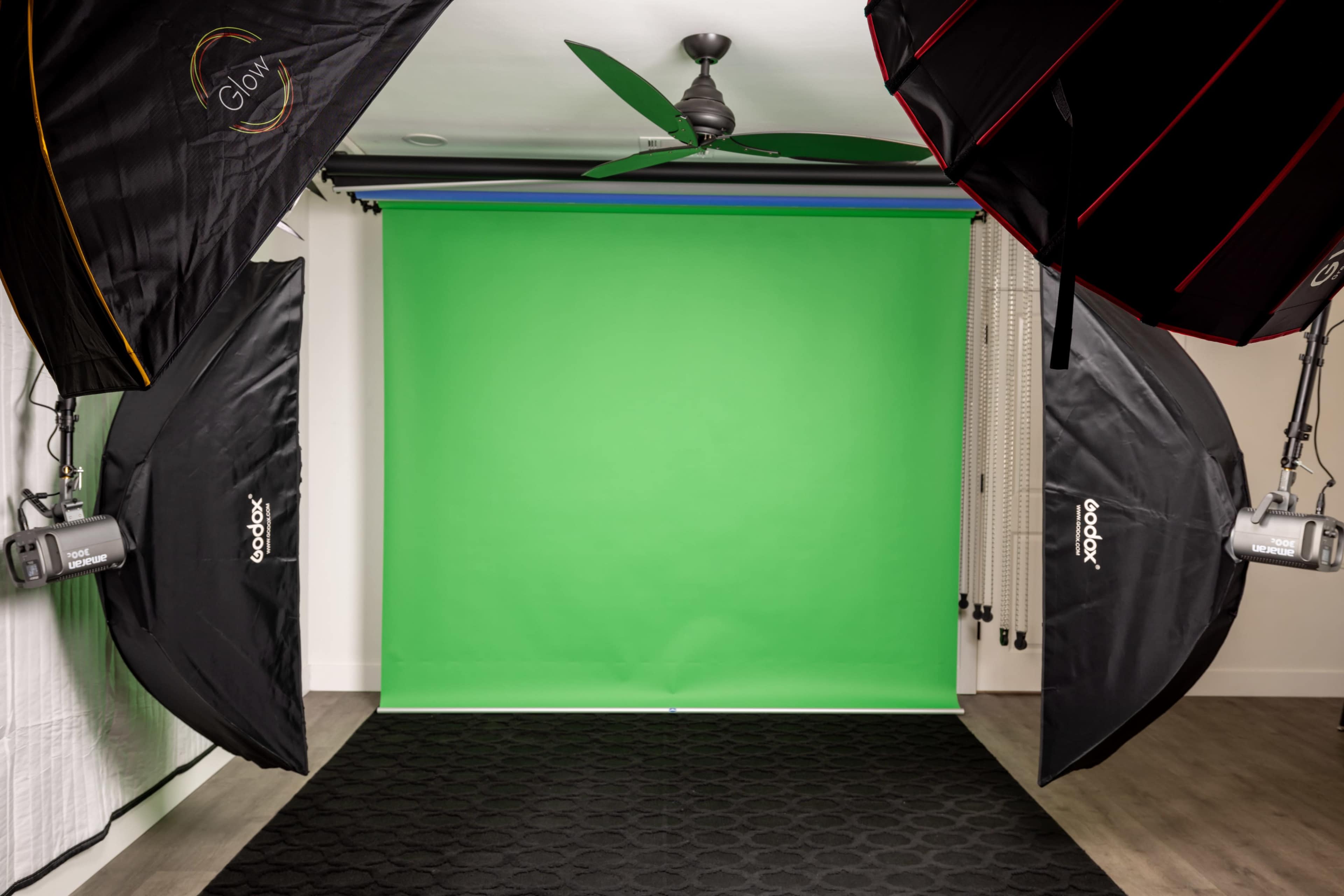 The image shows a photography studio setup featuring two softbox lights, a green backdrop, and a dark carpet.