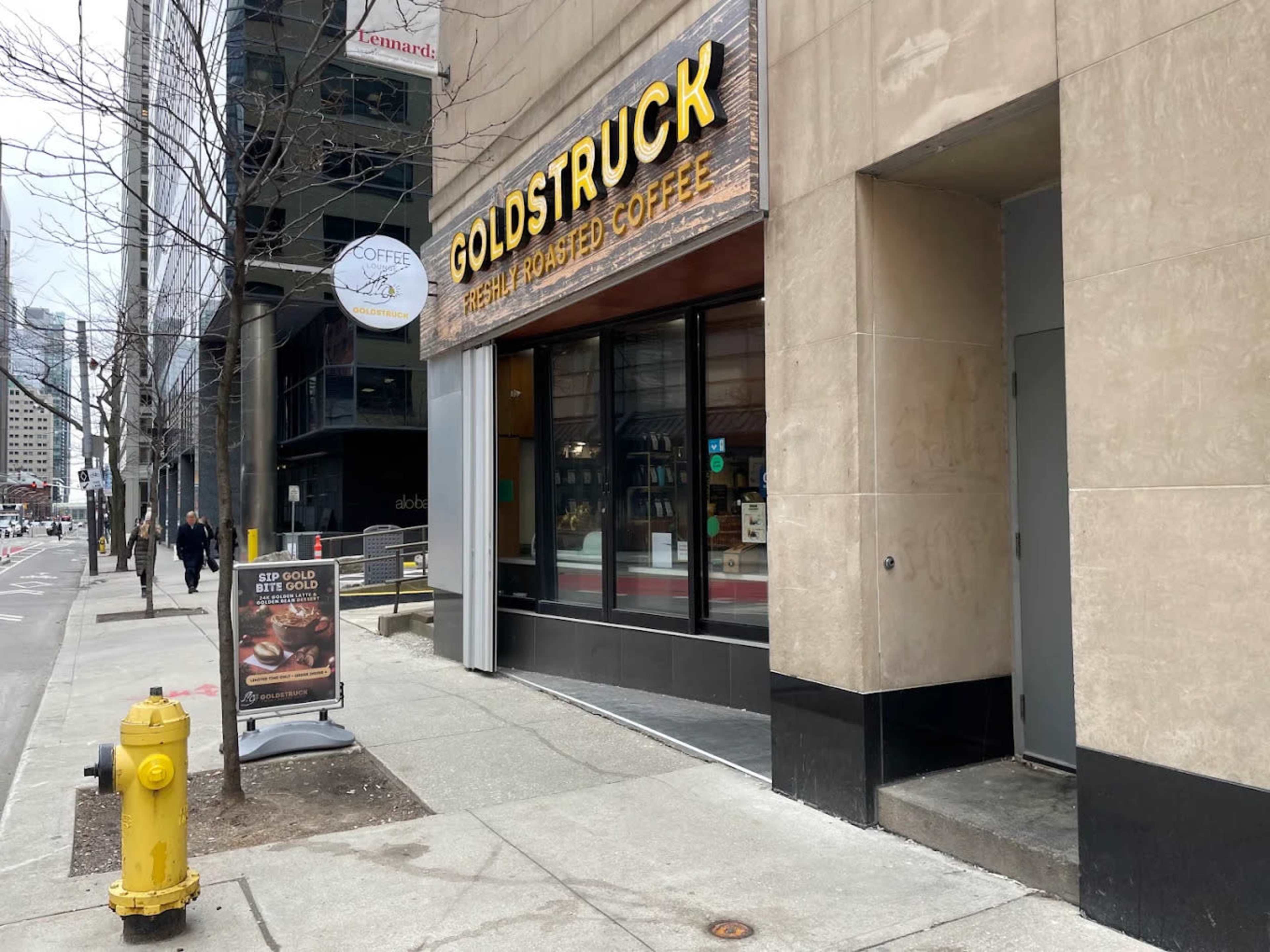 The image shows a coffee shop named "Goldstruck" with a sign displaying its specialty in freshly roasted coffee, located on a city sidewalk near a fire hydrant.