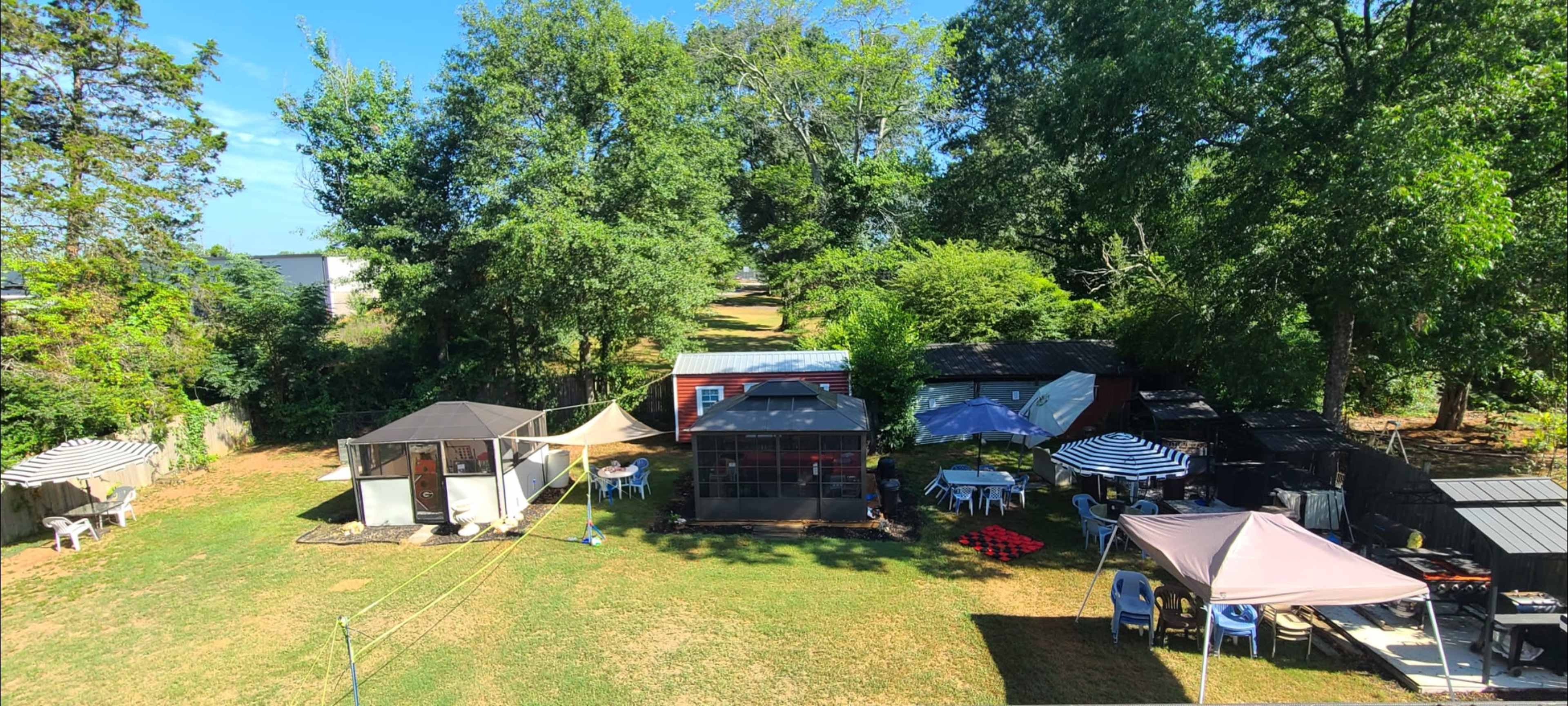 A backyard with several tents and tables set up among green grass and trees.
