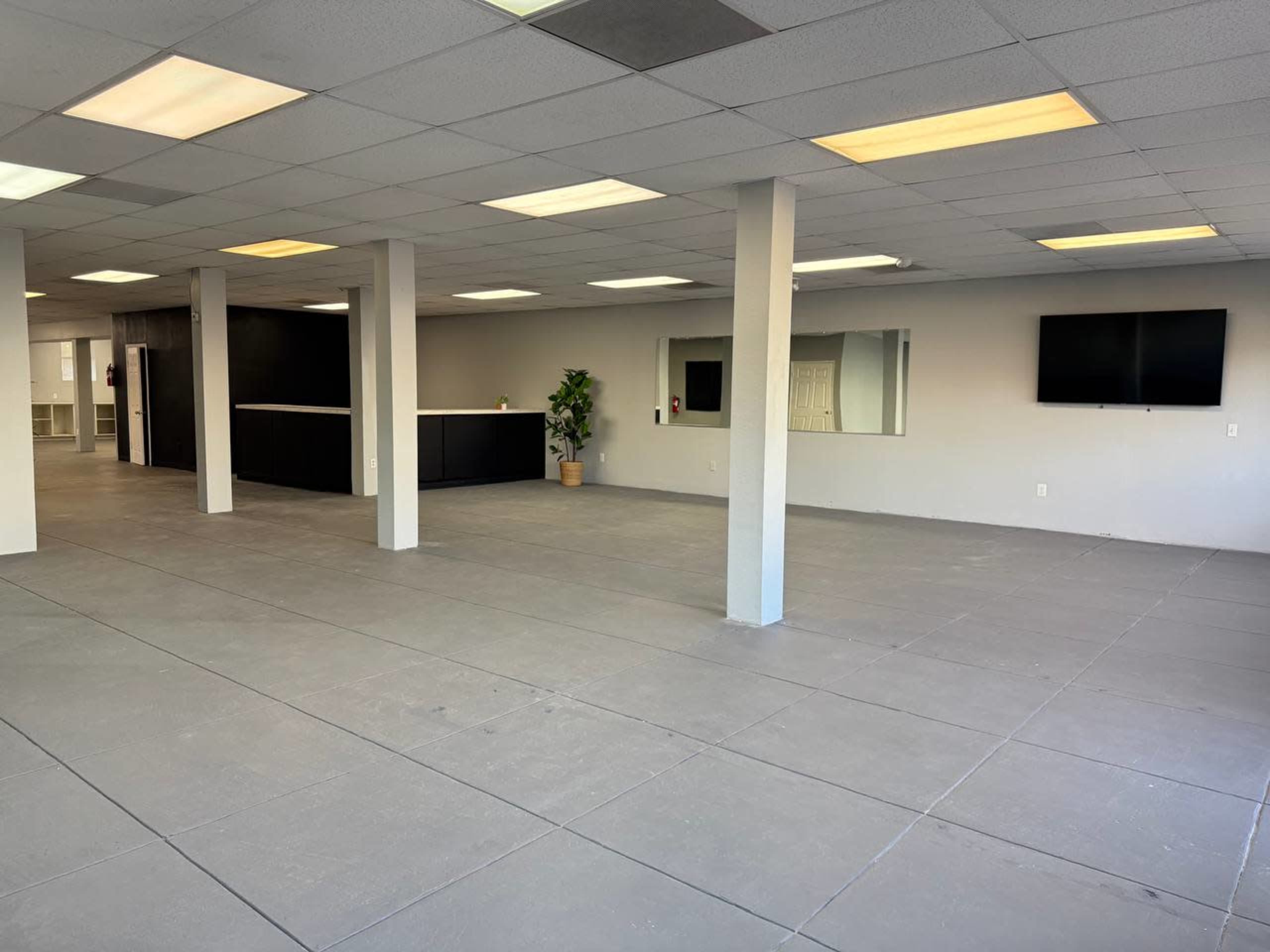 The image shows an empty commercial space with gray concrete flooring, white walls, and a reception or counter area in the background.