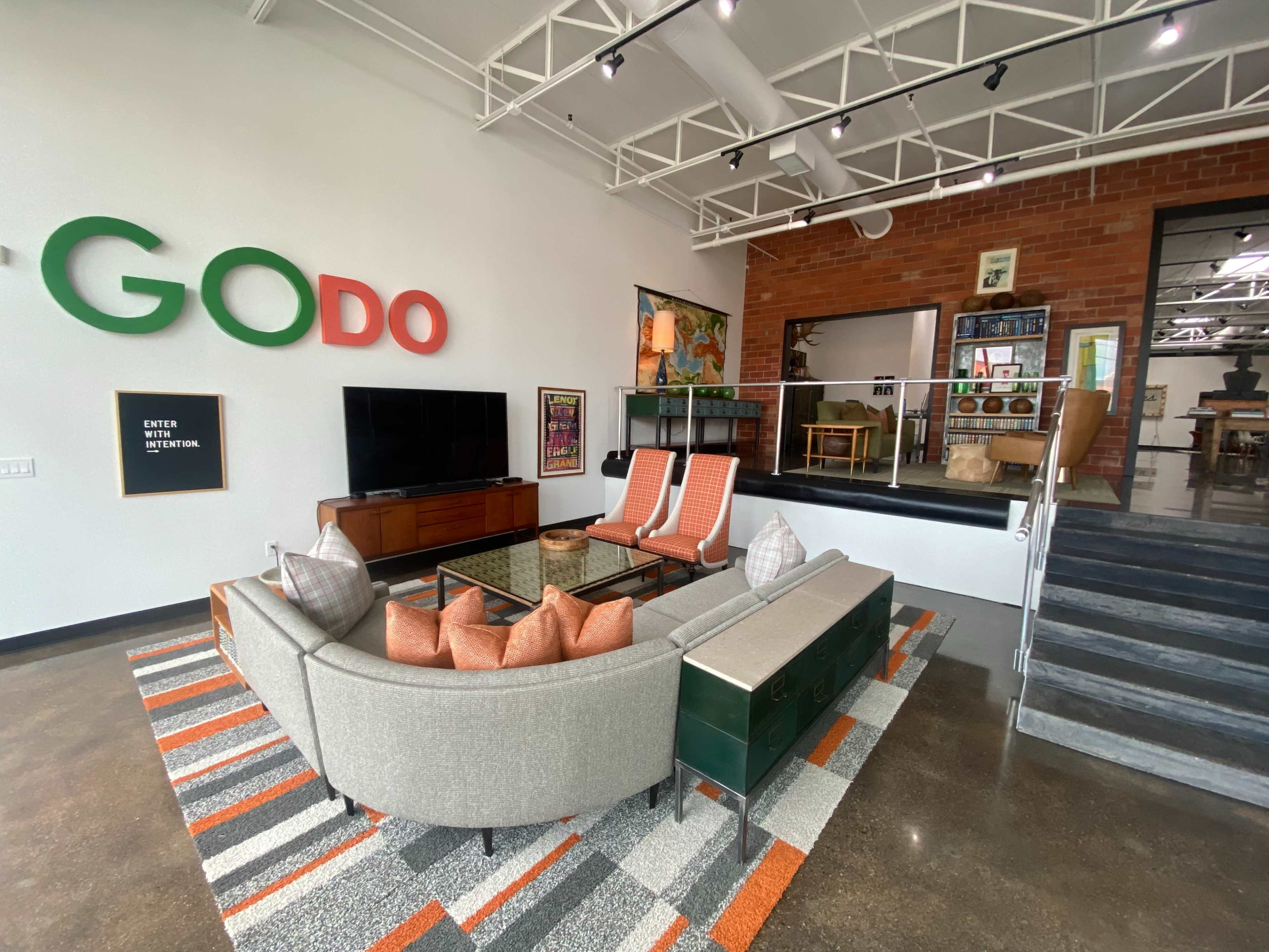 A modern living space with a gray sectional sofa, two orange chairs, a large TV, and a staircase leading to an elevated area.